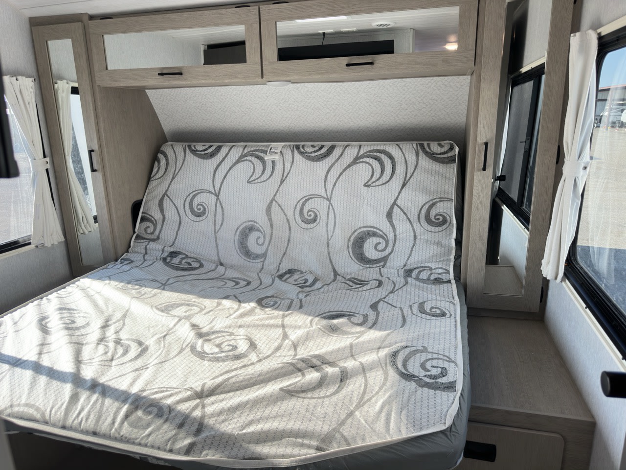 Explore this cozy RV rental bedroom. Features a patterned mattress, overhead storage, and natural light from side windows.. Forest River Wildwood Platinum 2024