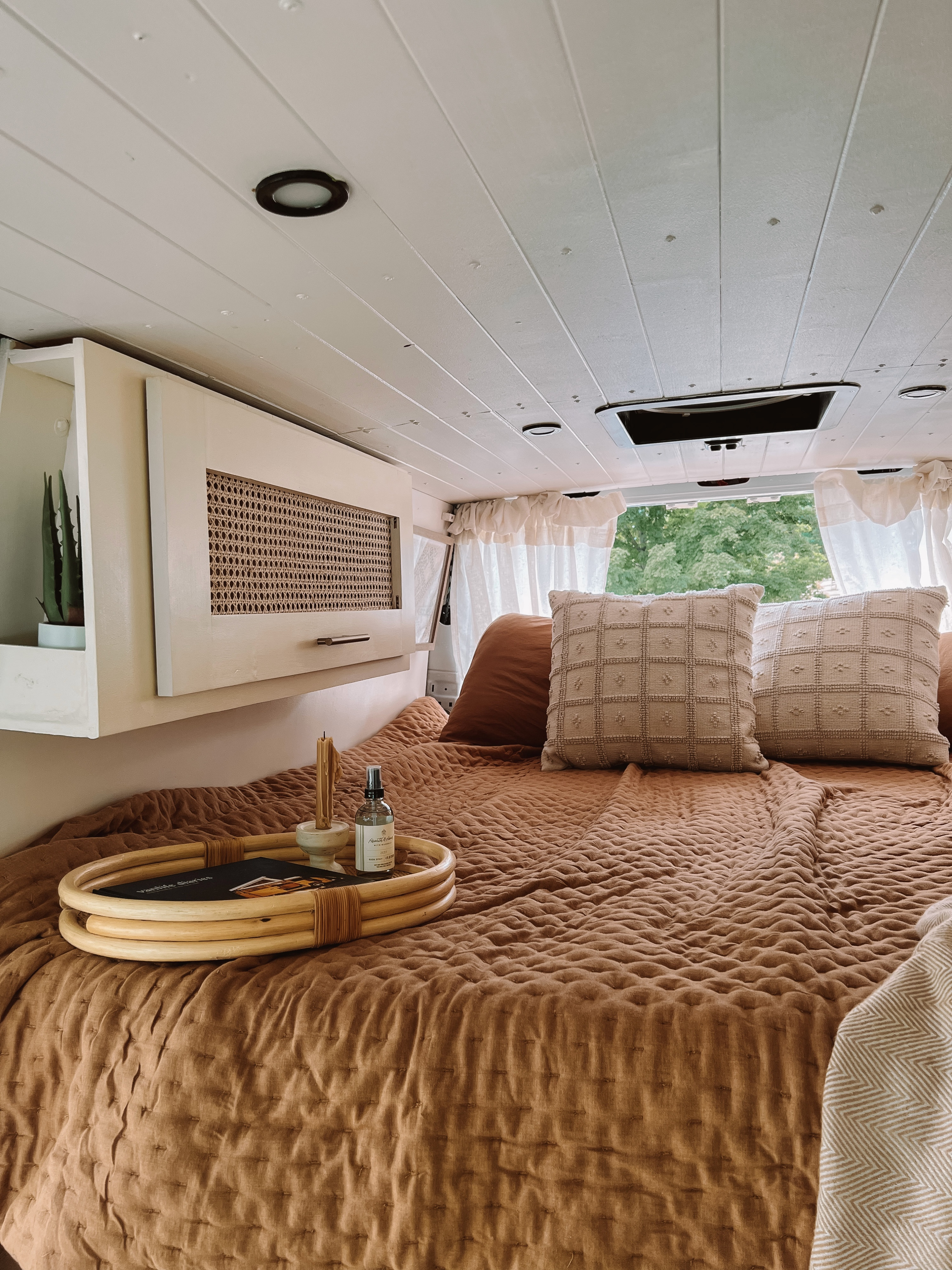 Bright RV rental interior: cozy bed with quilted cover, rattan cabinet, and nature view from the window.. Mercedes-Benz Sprinter 2013