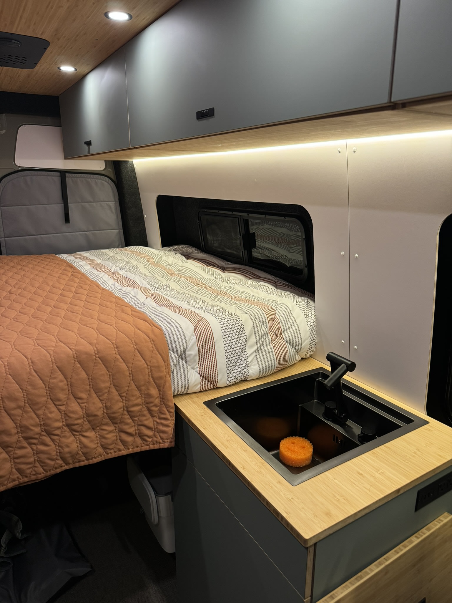 Cozy RV rental interior with a comfortable bed, compact sink, and overhead cabinets, ideal for travel.. Geotrek Geotrek Class B 2024