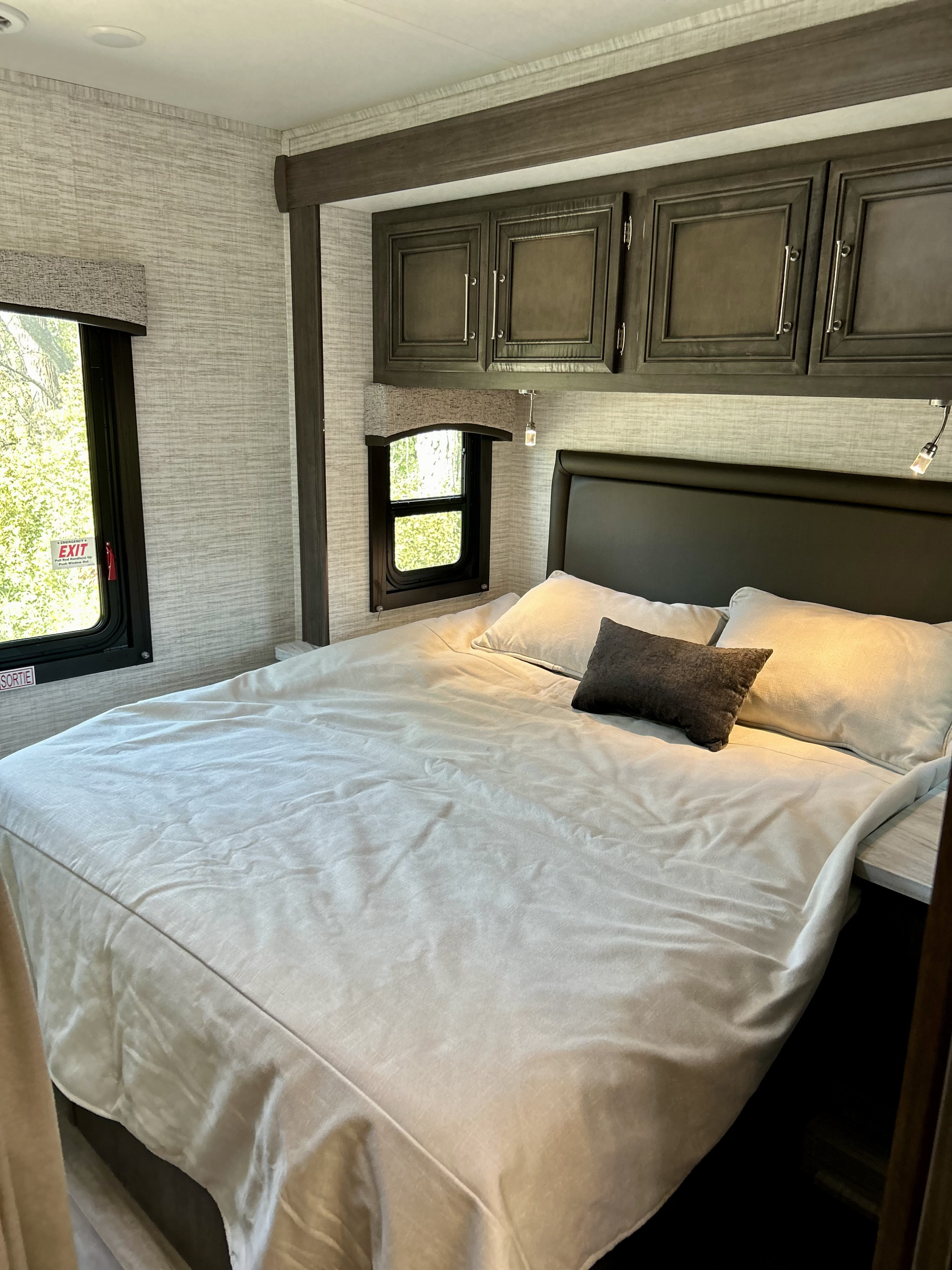 Cozy RV rental bedroom featuring a comfortable bed, dark wood overhead cabinets, and an emergency exit window.. Entegra Coach Odyssey SE 2024