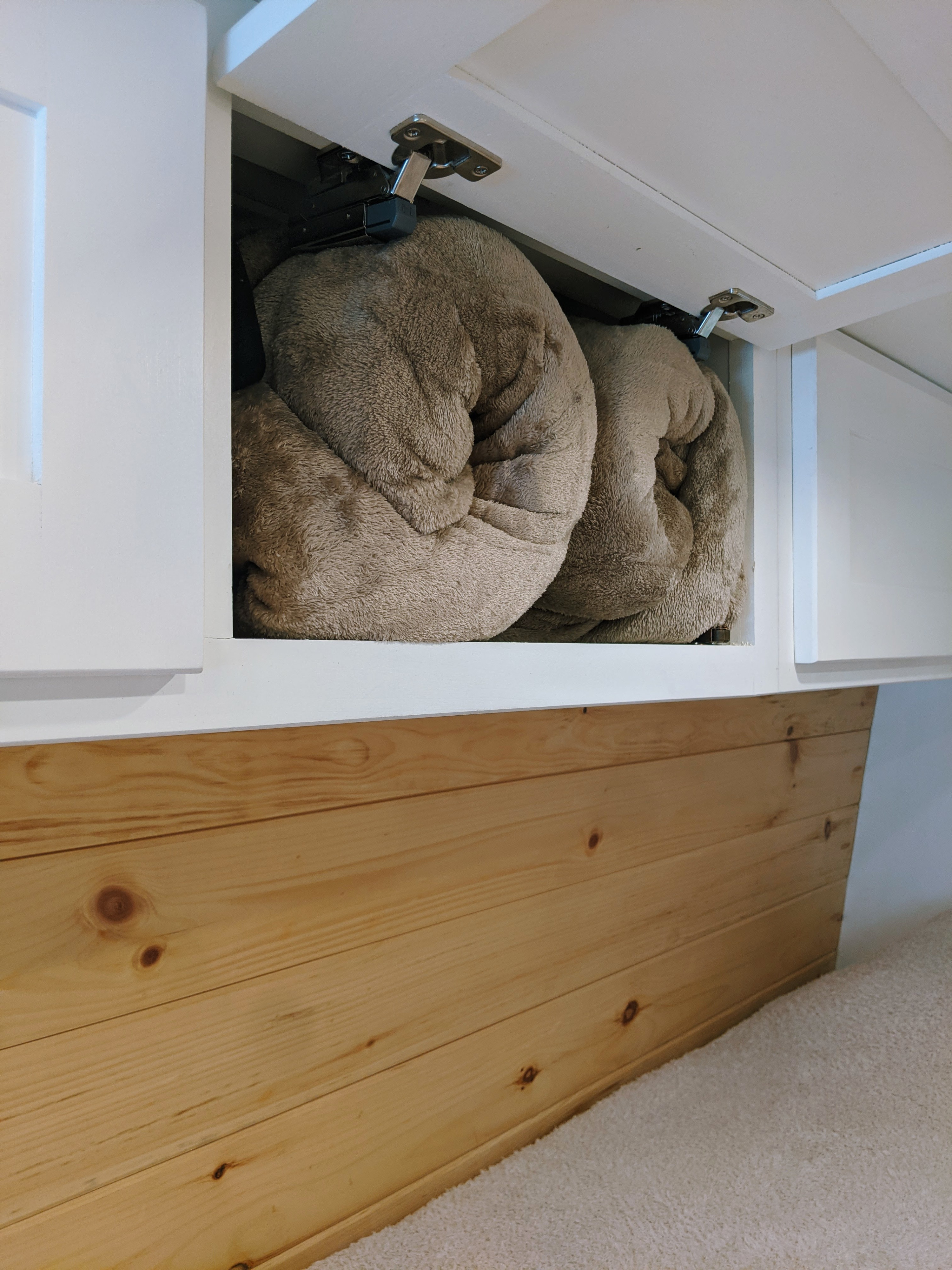 RV rental organized storage: Two soft, rolled blankets neatly inside an overhead white cabinet, above natural wood paneling.. Sprinter Mercedes 2018