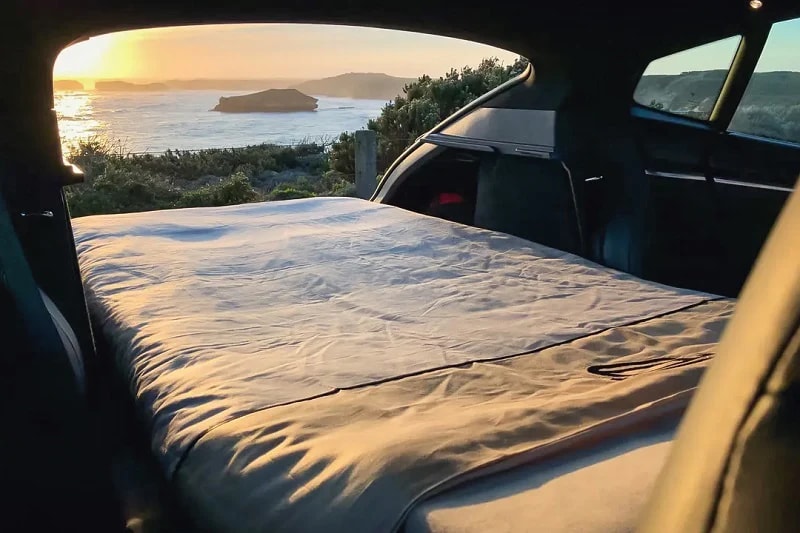 Mobile bedroom with ocean views! This car camping setup, a comfy alternative to an rv rental, features a bed overlooking a sunset coast.. Tesla Model Y 2021