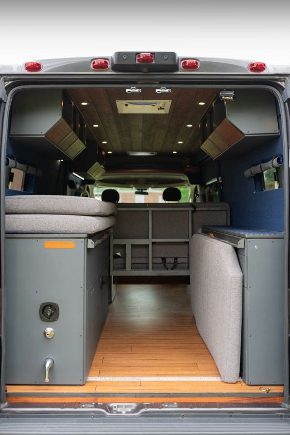 View inside a modern RV rental camper van, showcasing modular bed, storage, wood floor, and overhead compartments.. Beartooth Log Cabin 2018