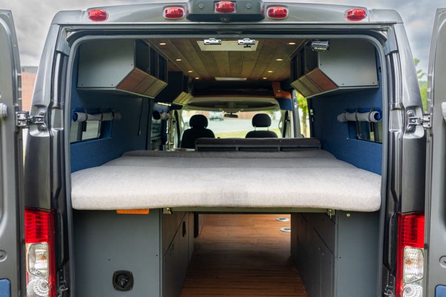 This RV rental showcases a camper van's interior with a comfy bed, wood floor storage, and overhead cabinets for adventure.. Beartooth Log Cabin 2018