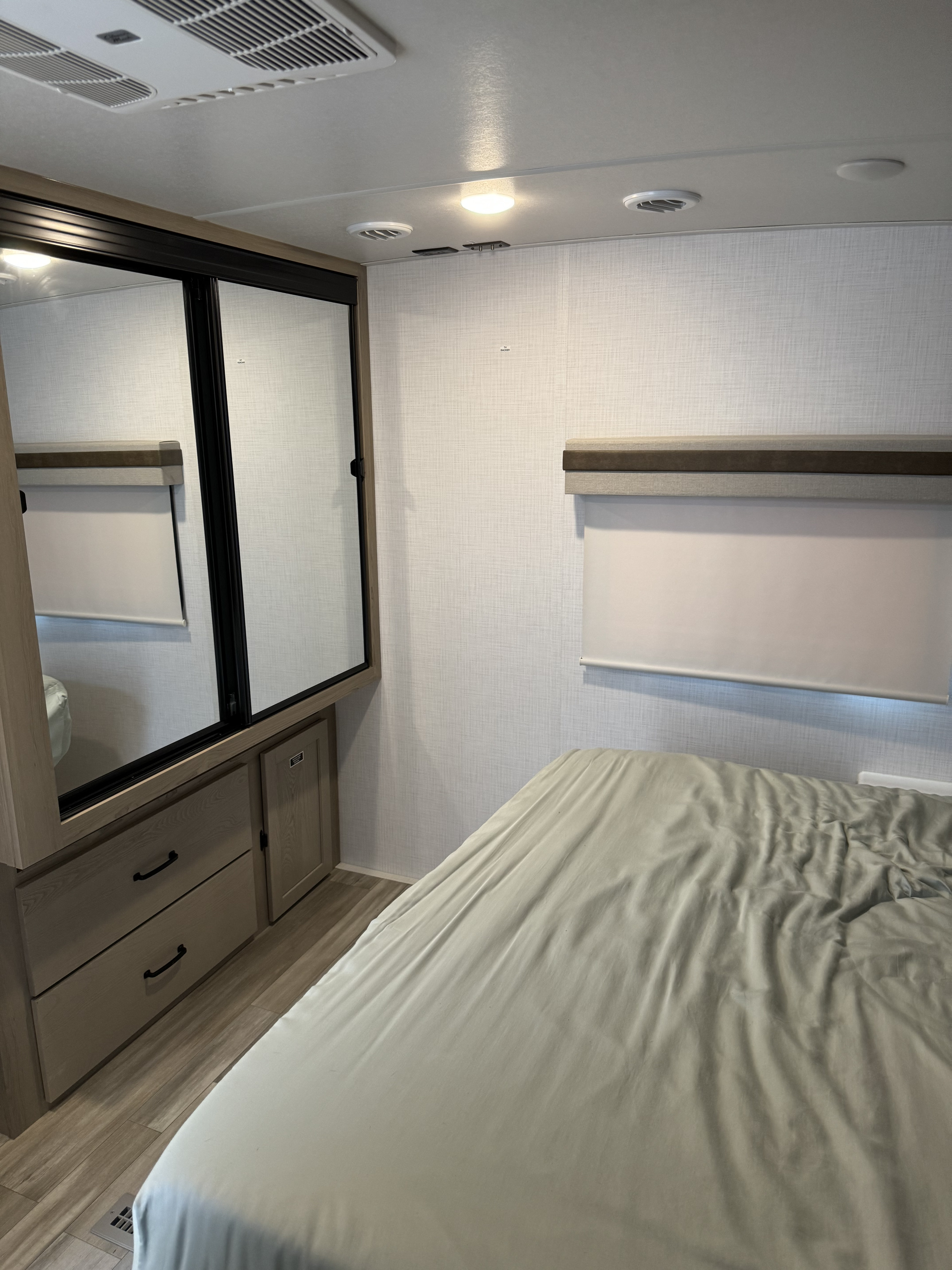 RV rental bedroom interior: light bedding, mirrored closet with drawers, window with blind, and ceiling AC unit.. Forest River Rockwood Ultra Lite 2024