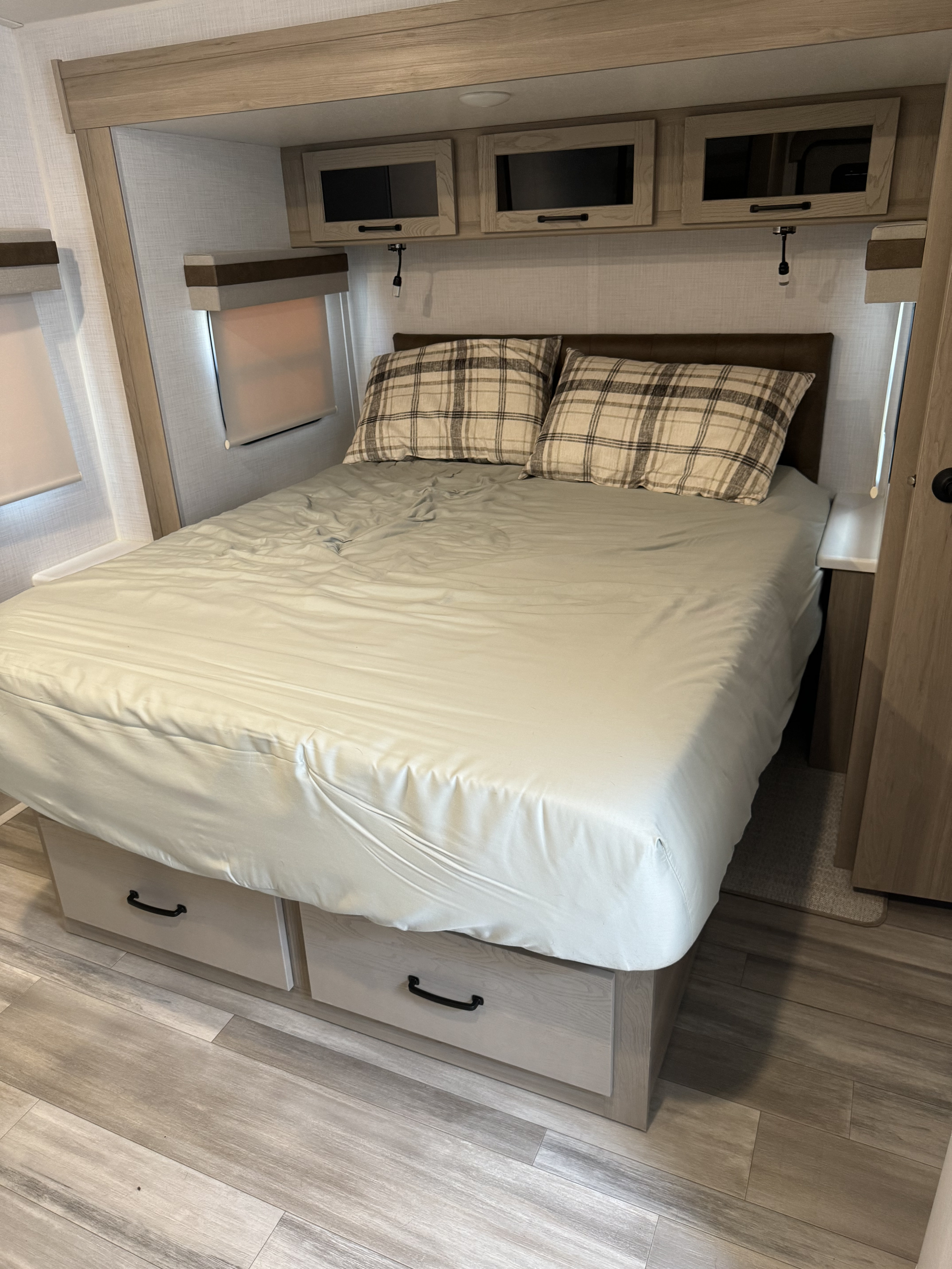 Comfortable RV rental bedroom with plaid pillows, overhead cabinets, and under-bed storage.. Forest River Rockwood Ultra Lite 2024