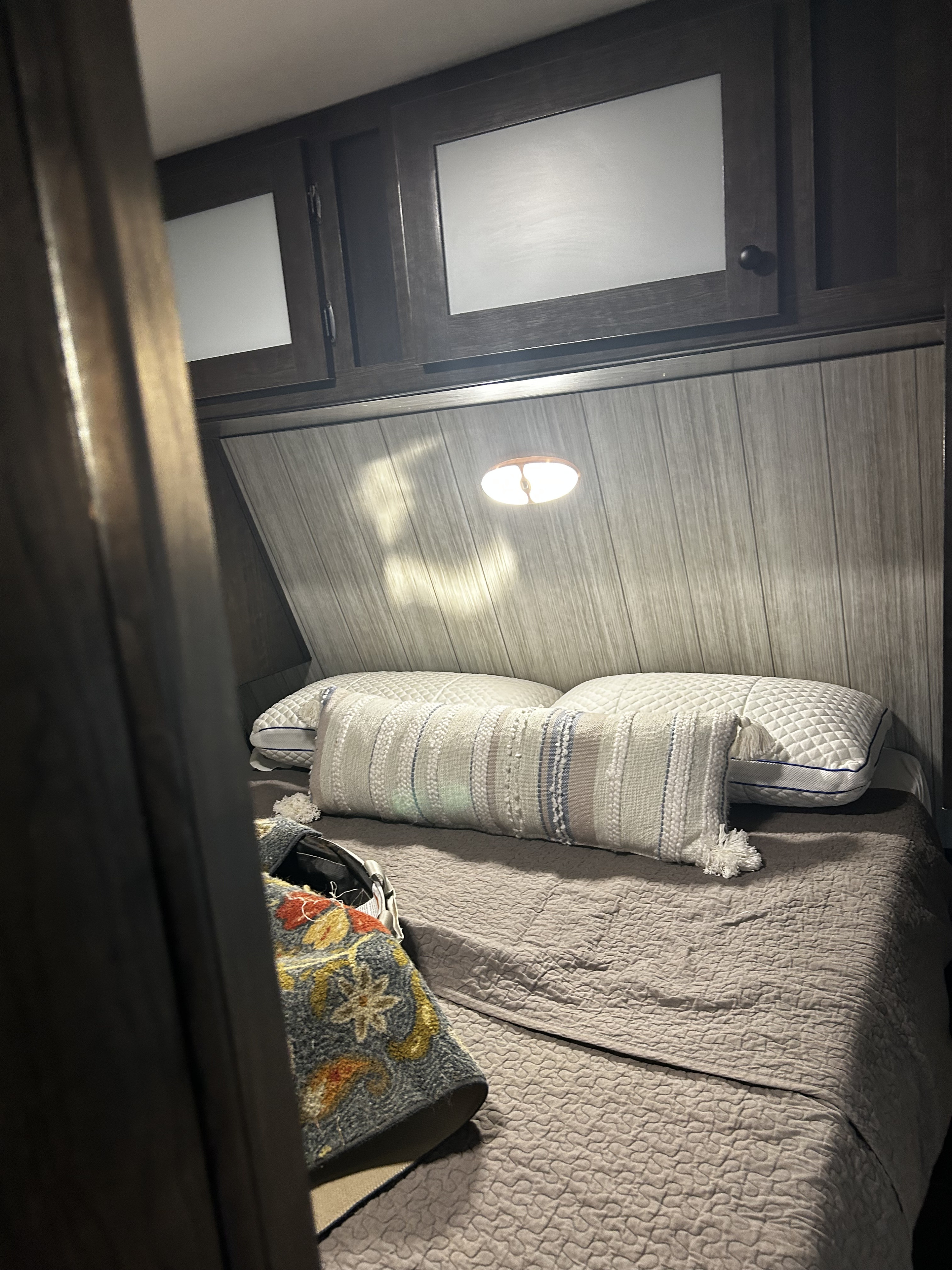 Cozy RV rental bedroom interior featuring a bed with quilted comforter and pillows, overhead light, and wall cabinets.. Heartland RVs Pioneer 2020