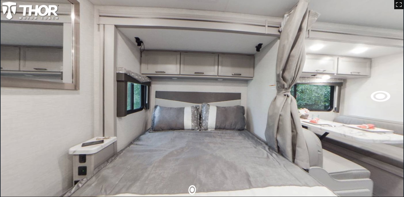 Inside this modern RV rental: a comfortable bedroom with bed, window, and storage cabinets, leading to a bright dining area.. Thor Four Winds 2023