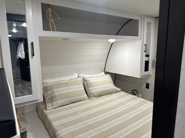 Step into comfort! This cozy RV rental bedroom features striped bedding, overhead storage, and a mirrored closet door.. Jayco Jay Flight 2024