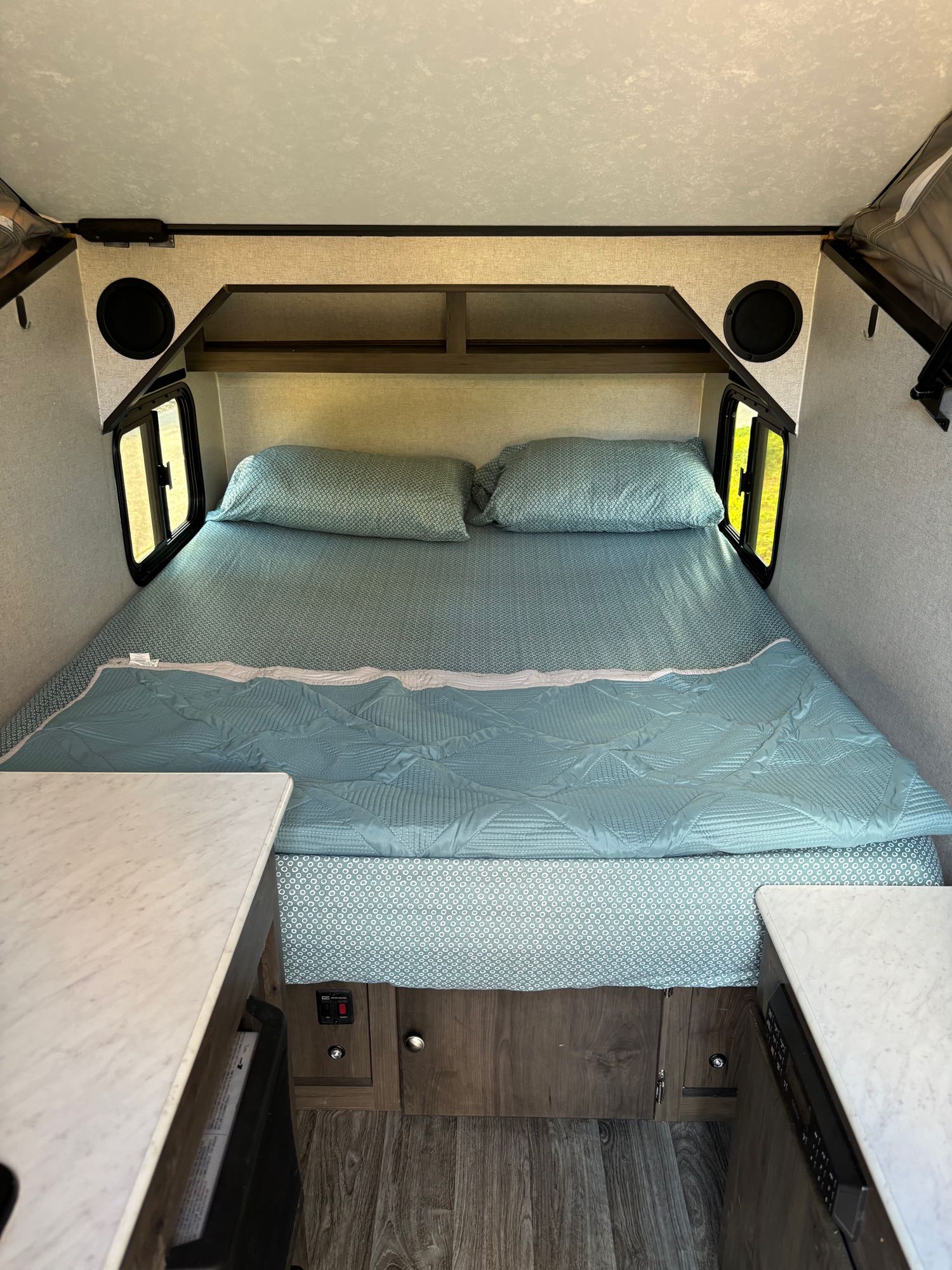 Cozy RV rental bedroom: large bed with light blue bedding, side windows, overhead shelves, and integrated speakers.. Forest River Viking 2020
