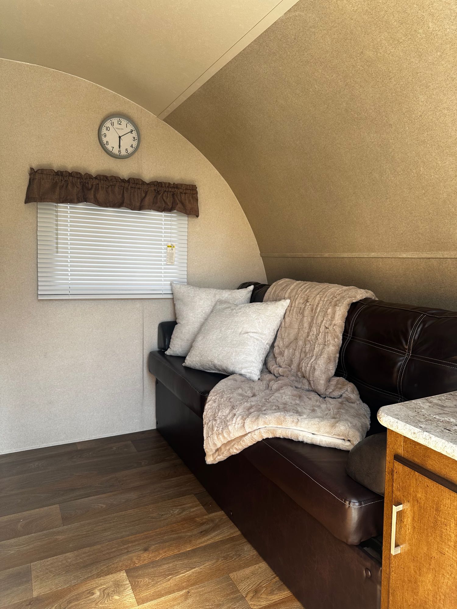 Cozy RV rental interior featuring a dark sofa, fluffy blankets, window with blinds, and wood floor.. Forest River Salem Cruise Lite 2018
