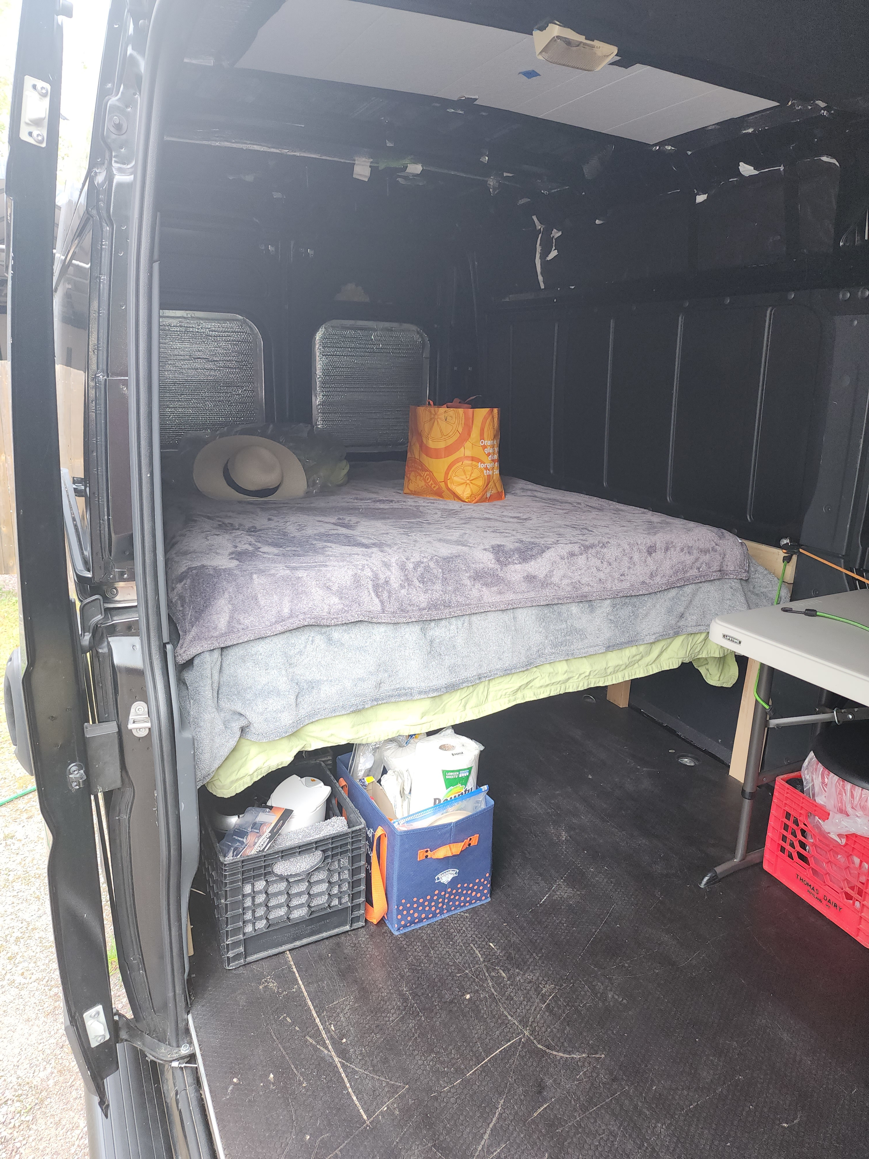 RV rental van interior showing a bed, under-bed storage crates with supplies, and a folding table setup for travel.. RAM PROMASTER HT 159 2021