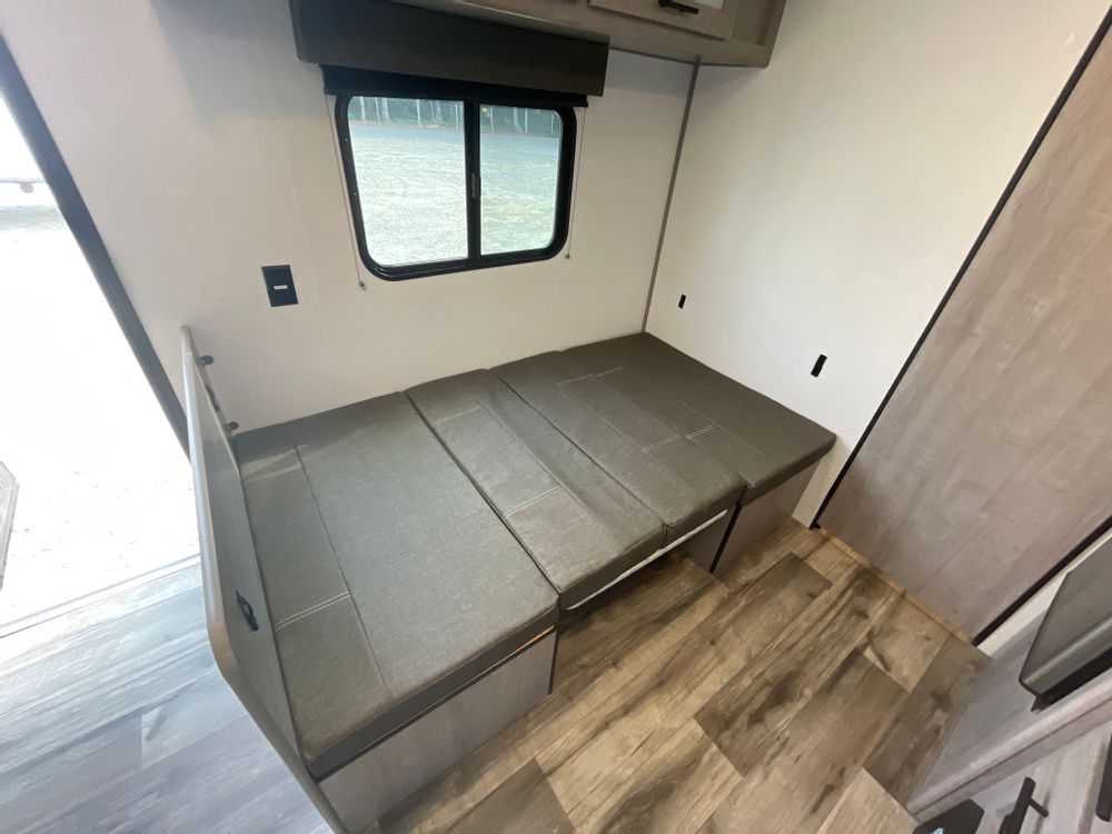 Inside an RV rental: versatile dinette seating converts to a bed, beside a window. Features wood-look flooring.. Coleman Lantern 2024