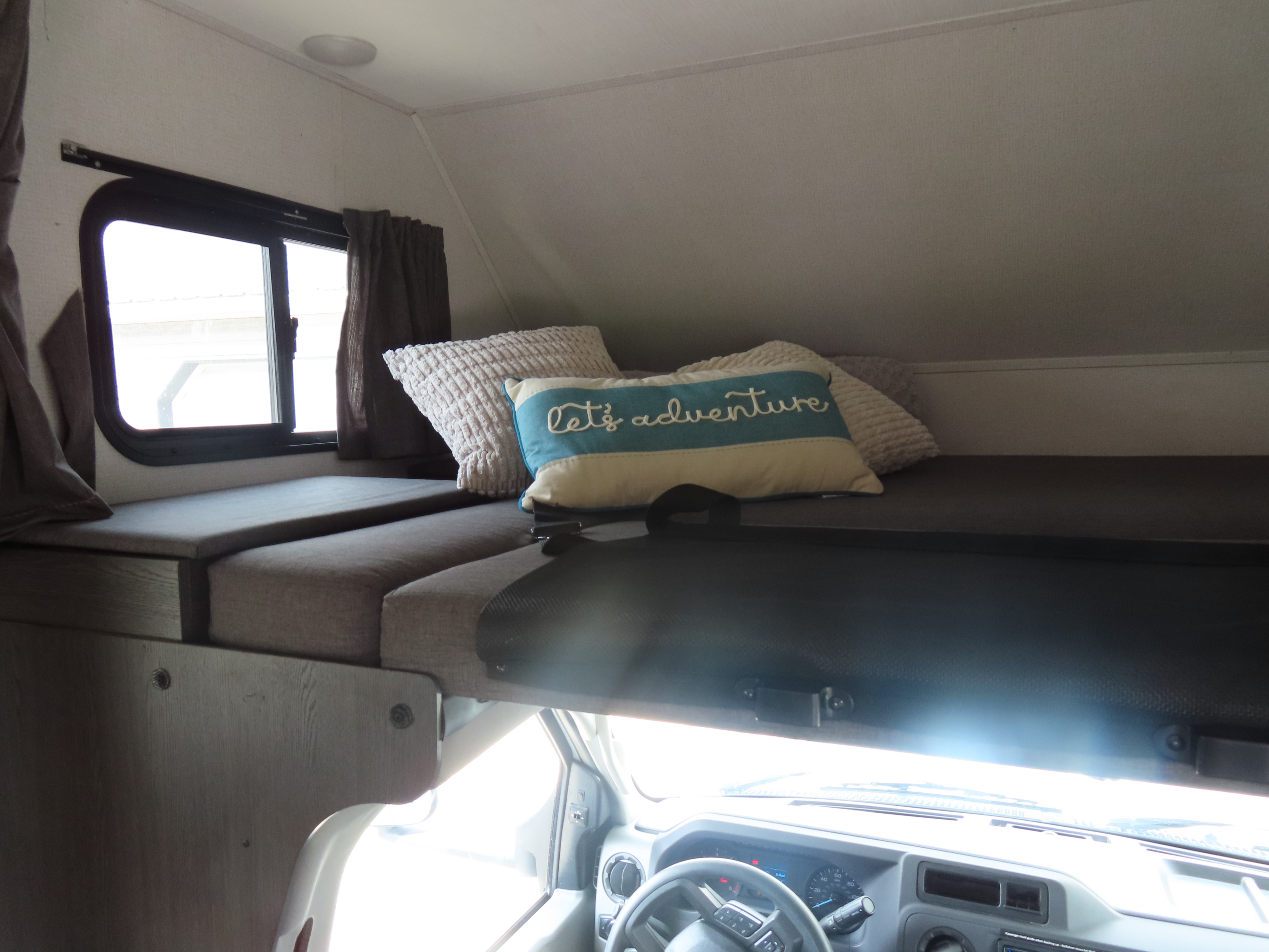 Cozy RV rental interior showing a comfortable cab-over bunk with pillows and the vehicle's driver's cockpit below.. Forest River Sunseeker LE 2022