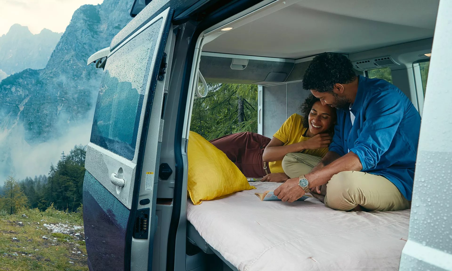 Comfy RV rental with a couple relaxing inside, admiring the misty mountain landscape through a wet window.. Volkswagen California Coast T6.1 4MO DSG7 204cv 2022