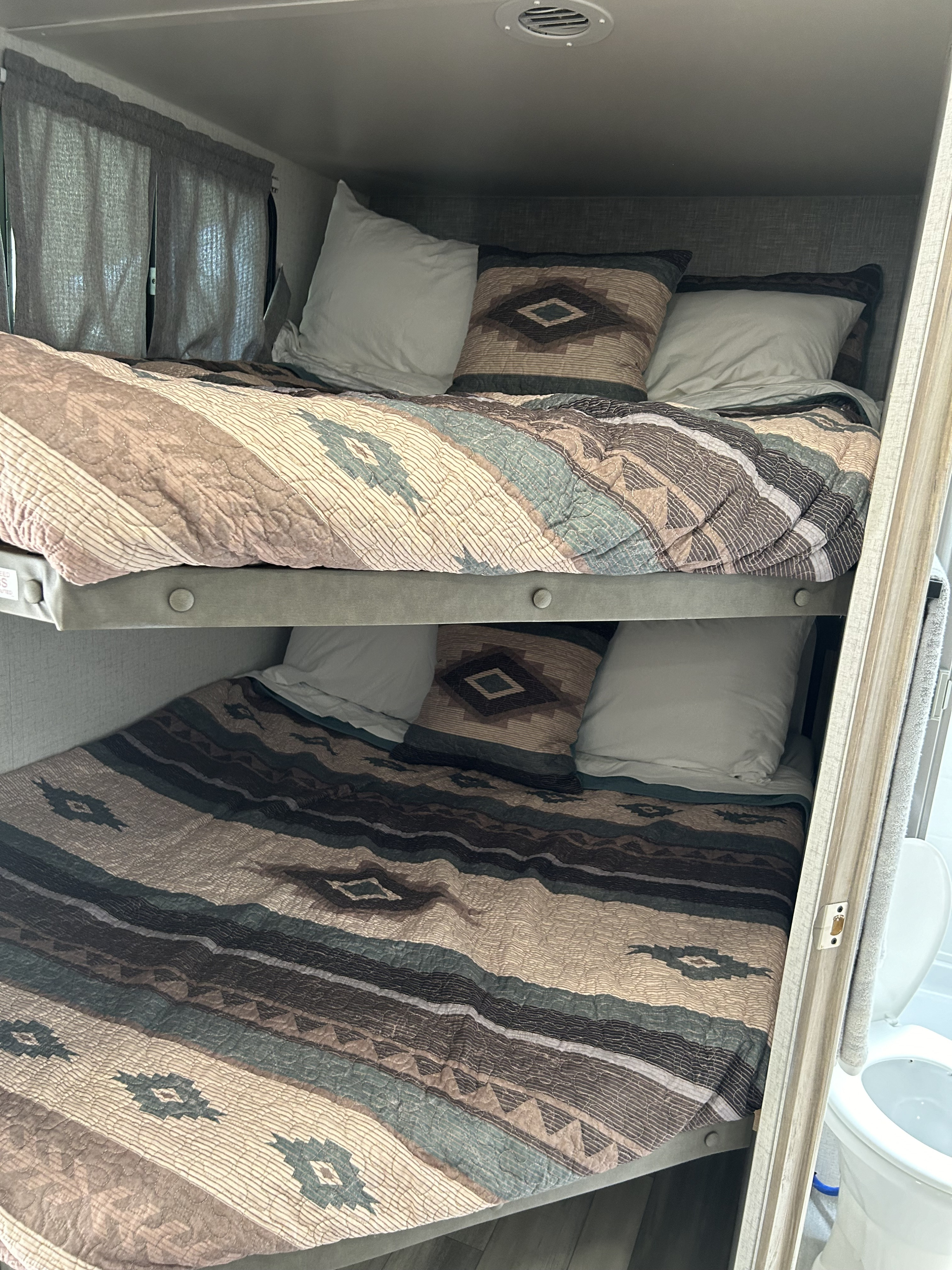 Cozy bunk beds with southwestern bedding in an RV rental. A toilet is partly visible, hinting at the compact interior.. Winnebago 2301bhs 2022