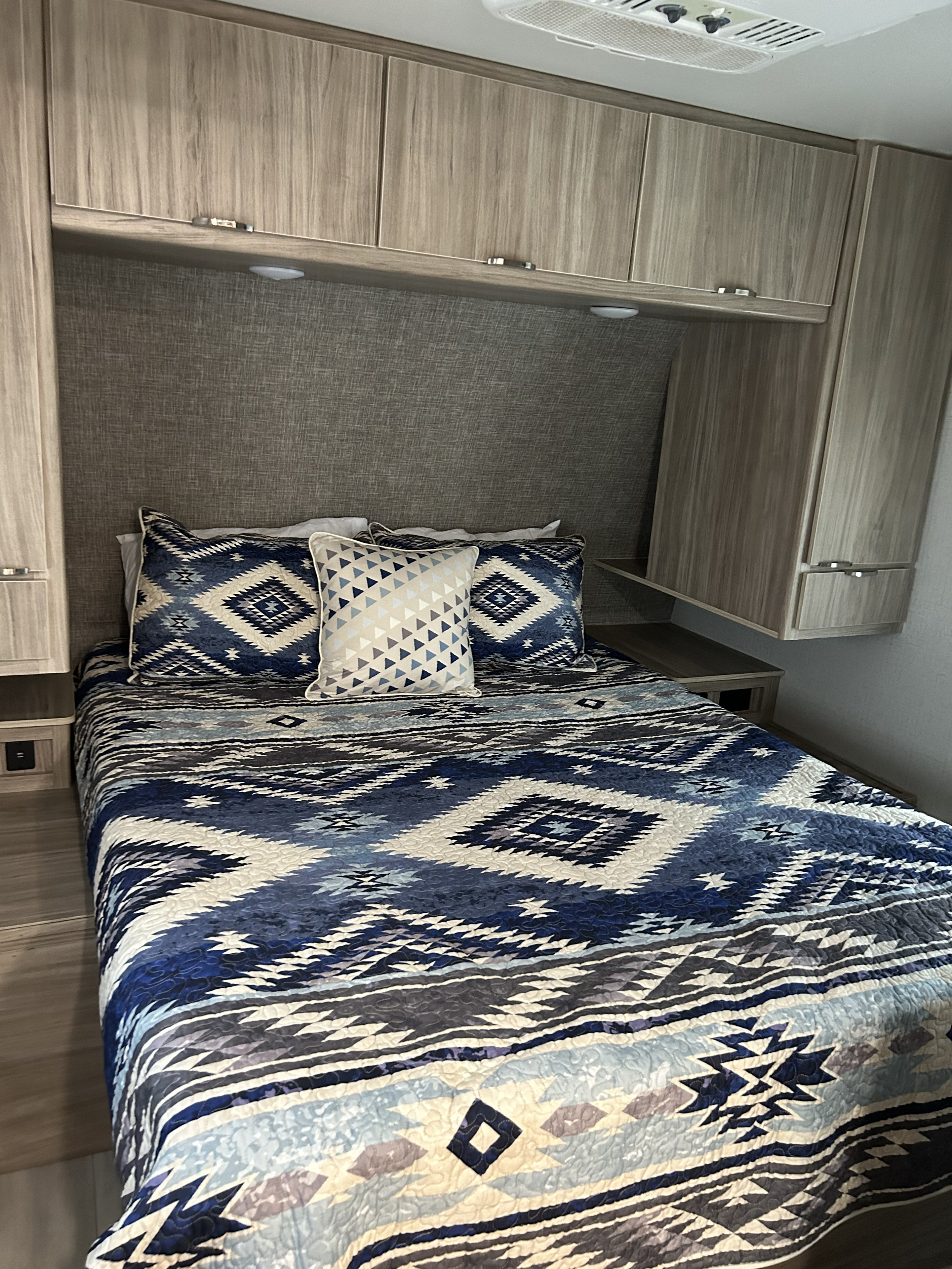RV rental bedroom: Features a comfortable bed with a blue patterned quilt, overhead cabinets, and built-in shelving.. Winnebago 2301bhs 2022