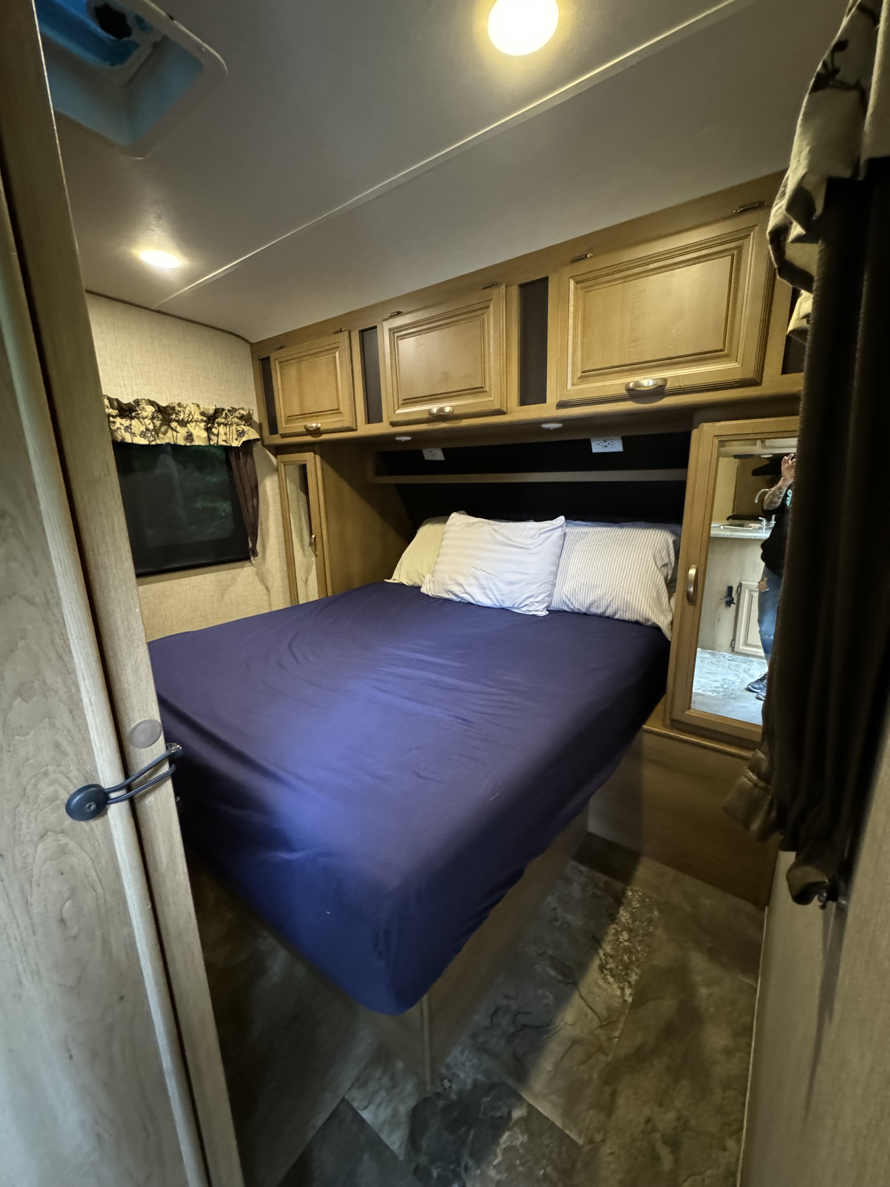 Inside this RV rental, find a compact bedroom with a blue-sheeted bed, overhead cabinets, and a mirror showing a reflection.. Crossroads RV Cruiser Aire 2016