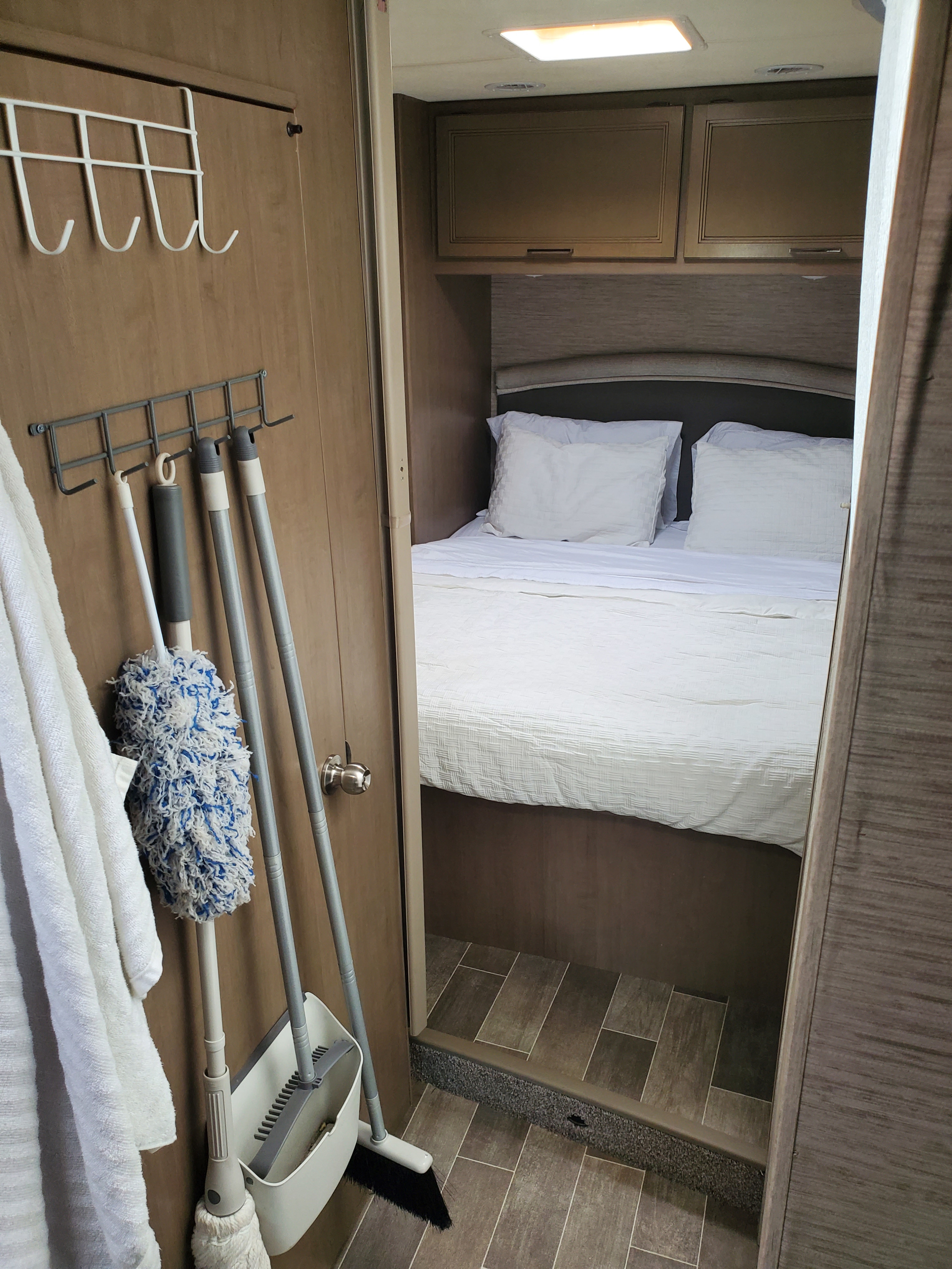Clean RV rental bedroom with white linens and practical storage for cleaning supplies, showing a comfortable space.. Thor Chateau 2021