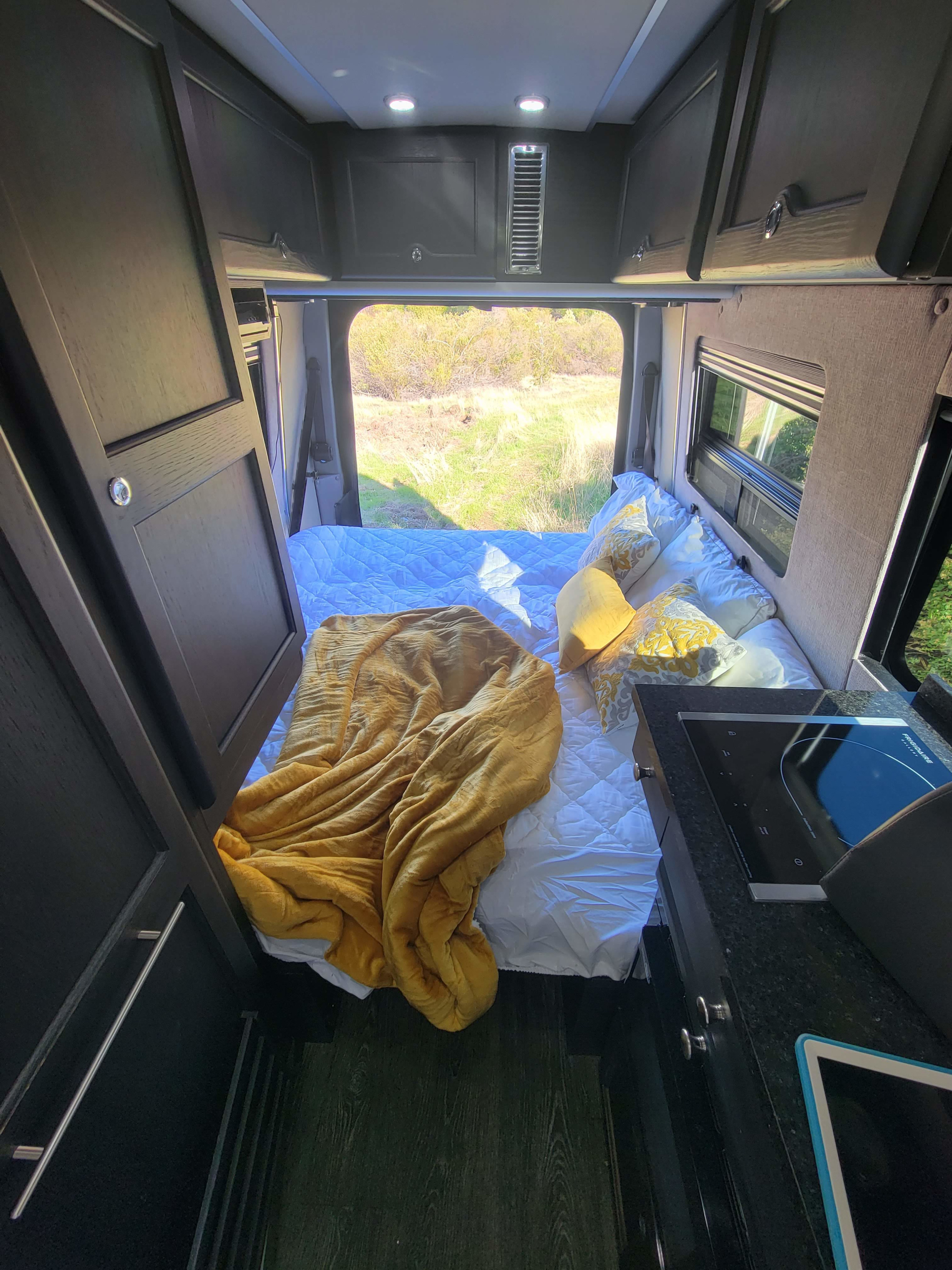 RV rental: a cozy interior featuring a bed with yellow accents, compact kitchen, and scenic nature view from the rear.. Roadtrek Roadtrek Class B 2017