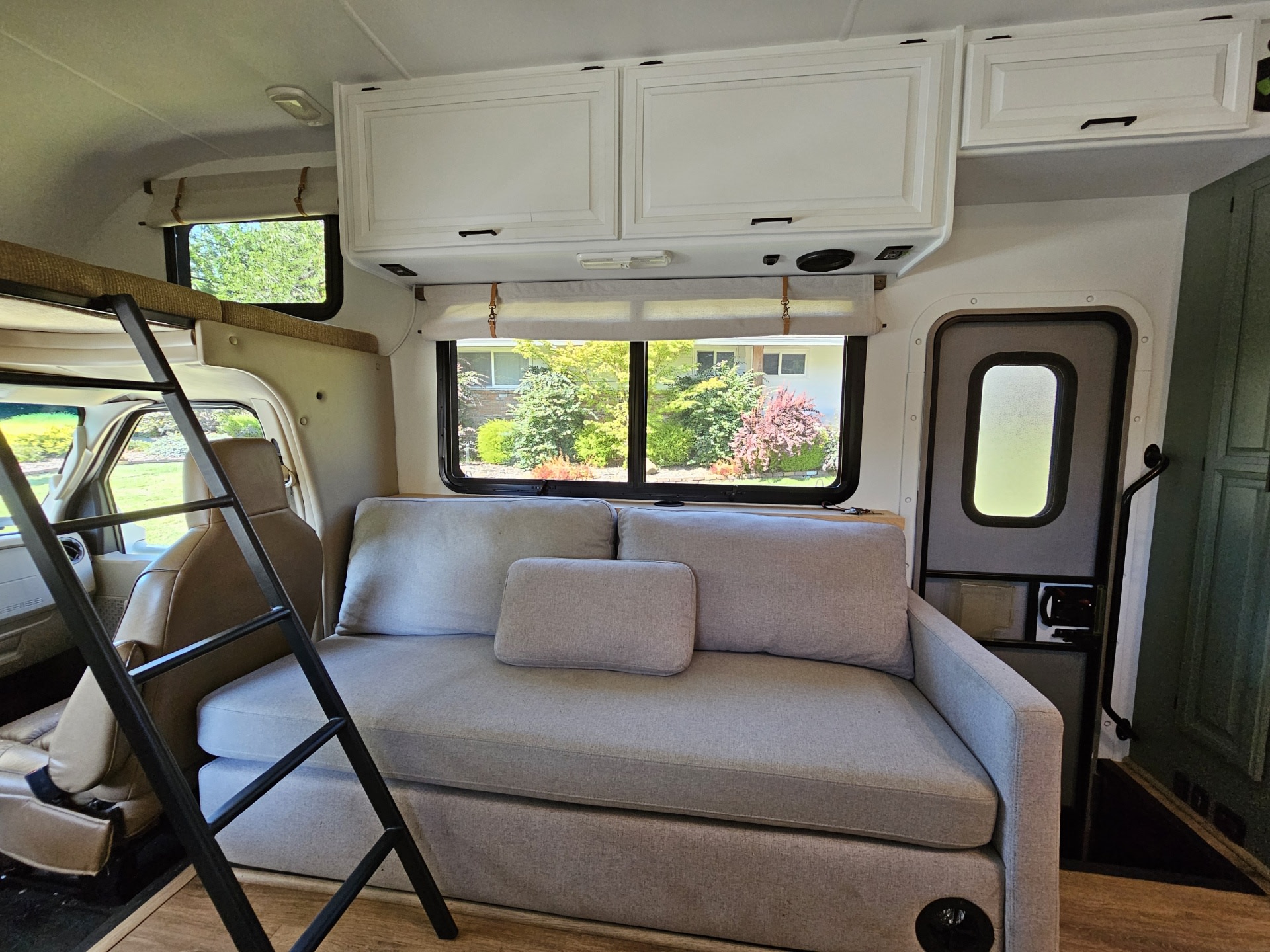Step inside this cozy rv rental, featuring a light gray sofa, bunk bed with ladder, white cabinets, and scenic window views.. Thor Four Winds 2015
