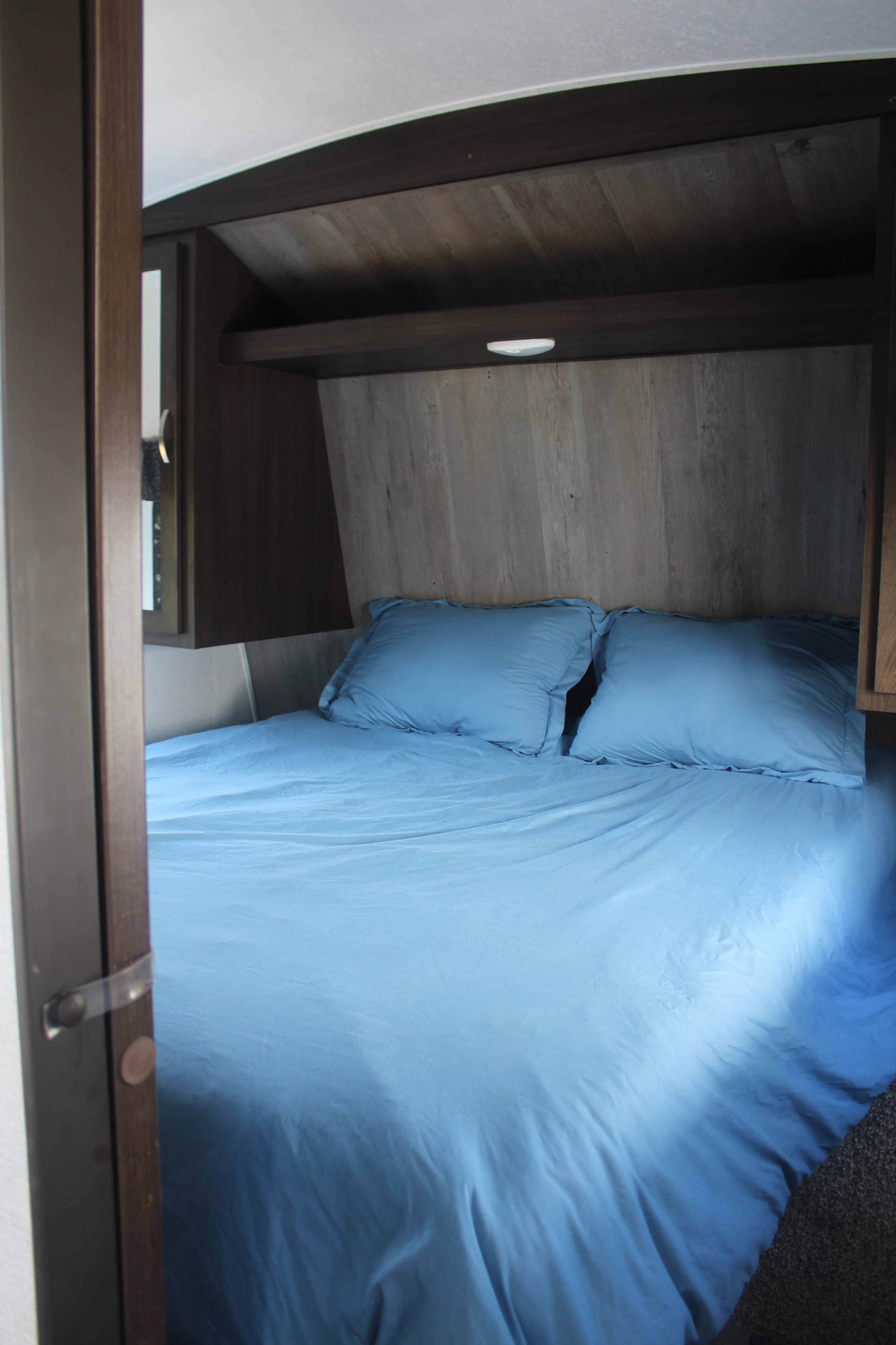 Comfortable RV rental bedroom featuring soft blue bedding and practical wood shelving.. Keystone RV Springdale 2020