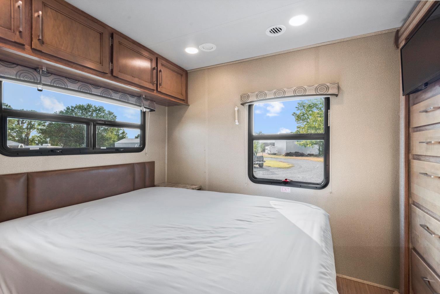 Comfortable RV rental bedroom interior with a large bed, windows displaying outdoor views, and storage.. Entegra Coach Odyssey 2020