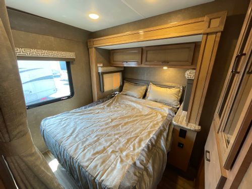 Cozy RV rental bedroom interior with a queen bed, overhead storage, and a window. Ideal for comfortable travel accommodations.. Thor Quantum 2018