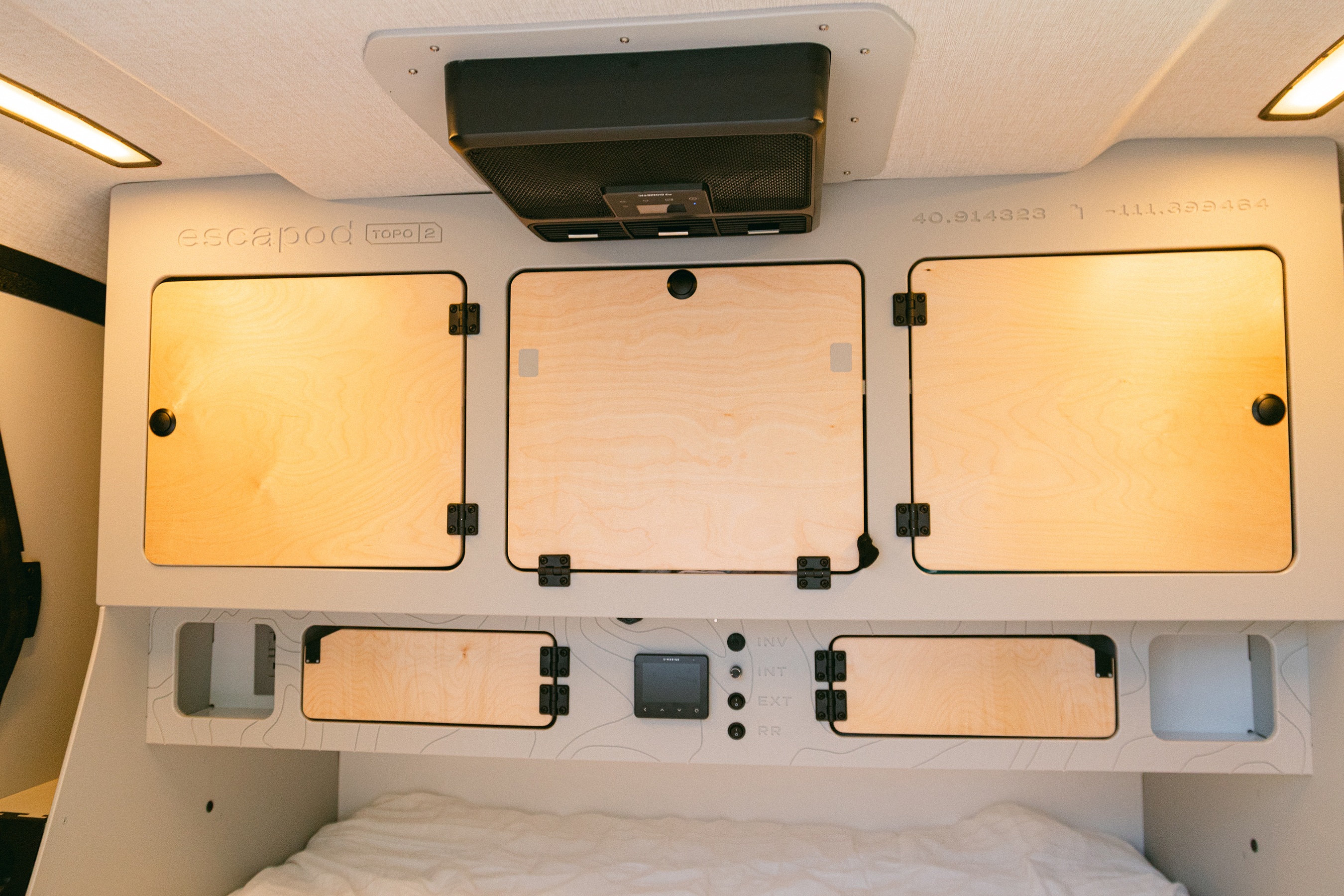 Modern Escapod rv rental interior with wooden cabinets, ceiling fan, and controls above a bed.. Escapod Topo 2 Voyager 2024