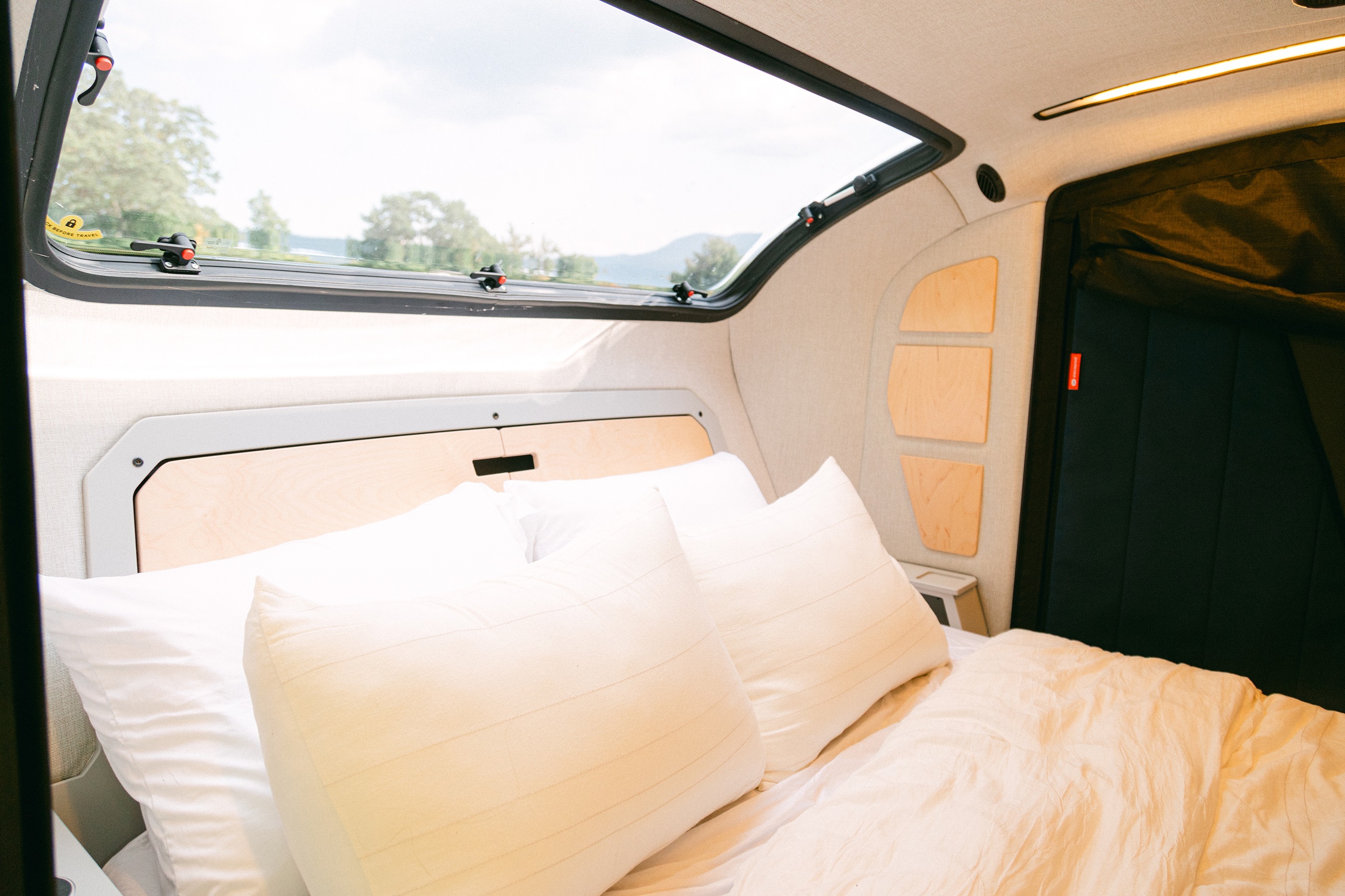 An RV rental's cozy interior features a comfortable bed, large window with a scenic view, and warm lighting.. Escapod Topo 2 Voyager 2024
