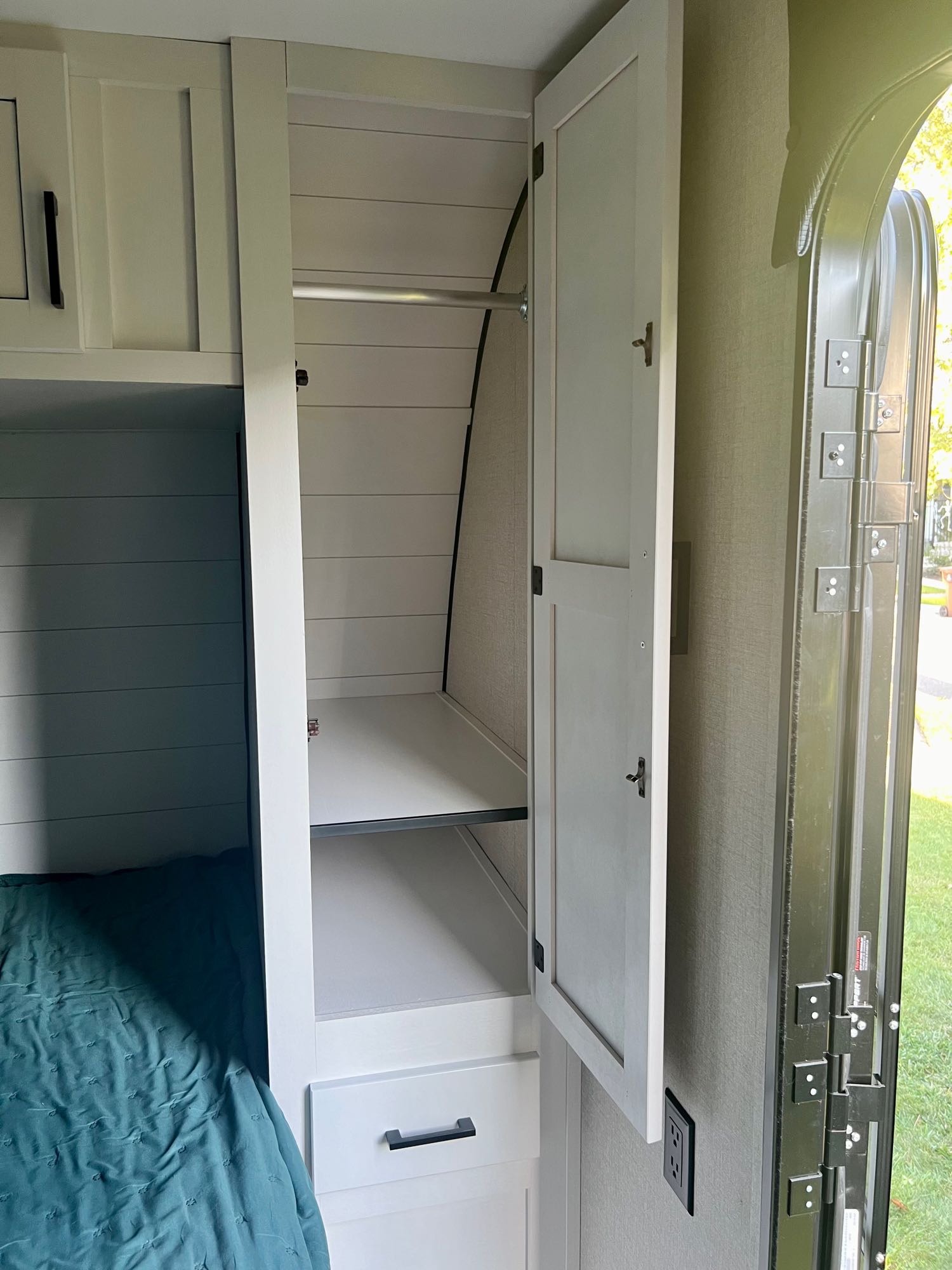 Spacious RV rental interior featuring an open wardrobe with hanging rod and shelves, plus a cozy bed.. Wayfinder GoPlay 19bh 2023