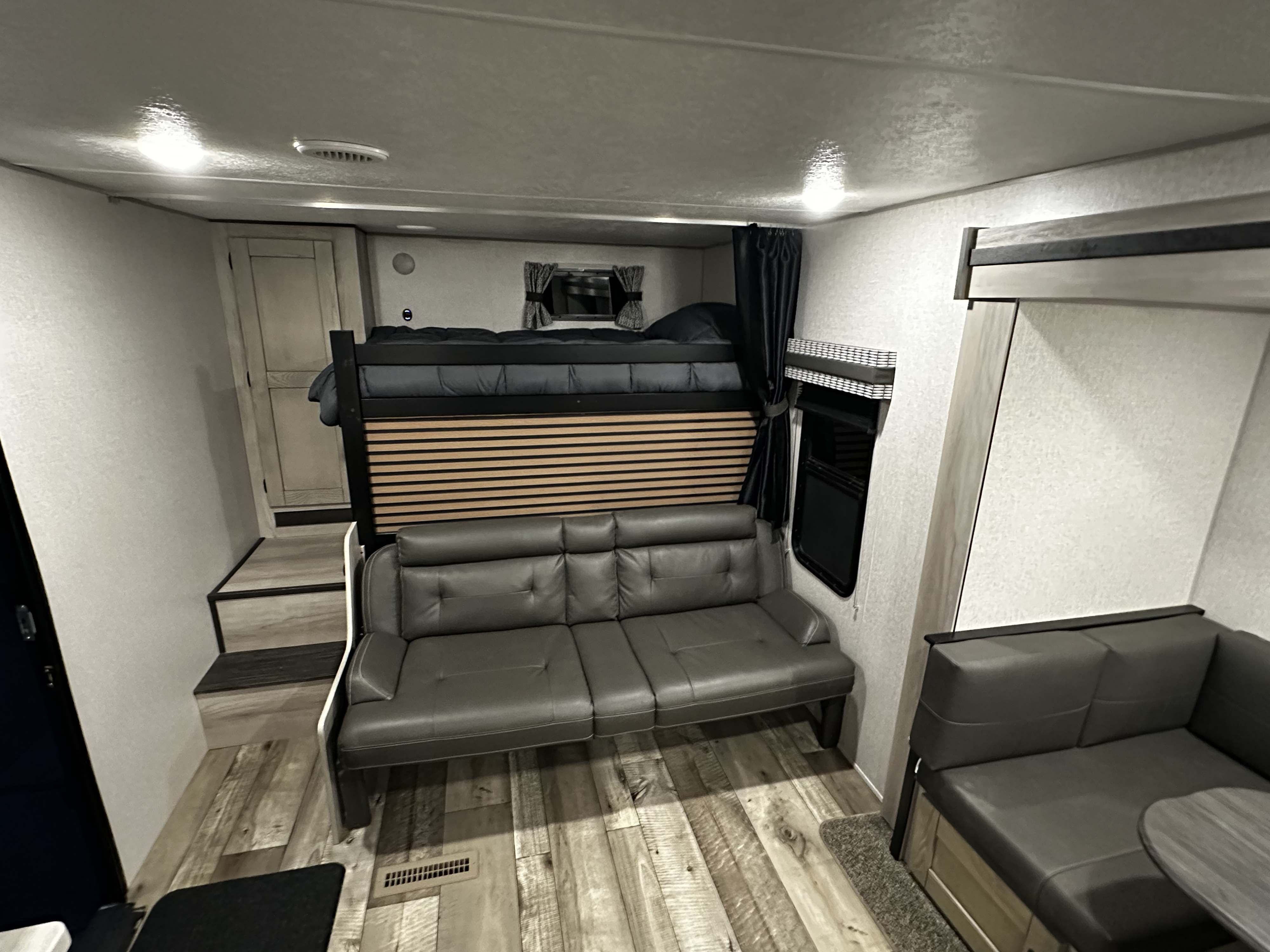 Spacious RV rental interior showing a bunk bed over a sofa, a dinette booth, and modern wood-look flooring.. Connect SE 2022
