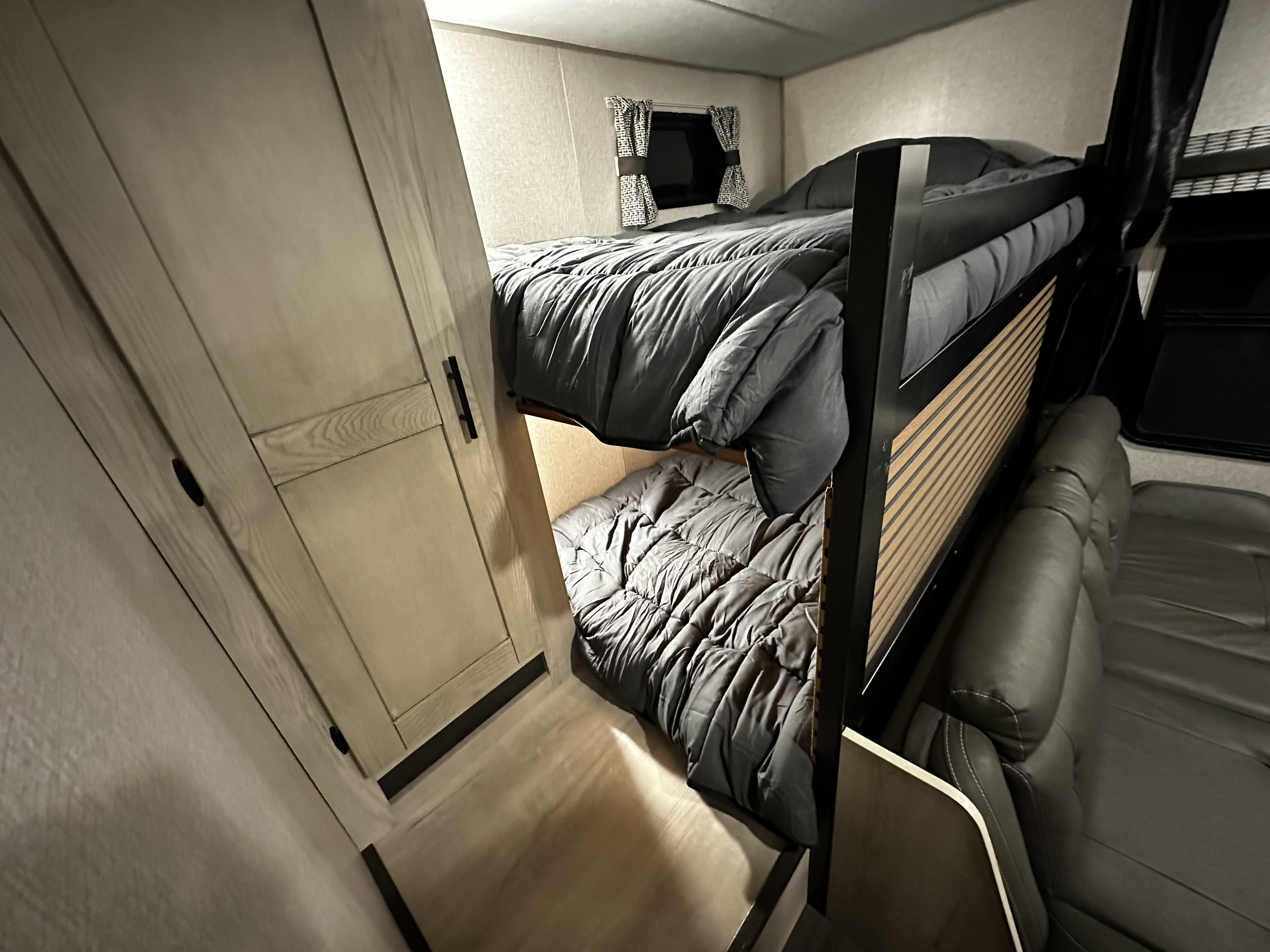 Cozy RV rental interior featuring bunk beds with grey comforters, a compact sofa, and light wood cabinetry.. Connect SE 2022