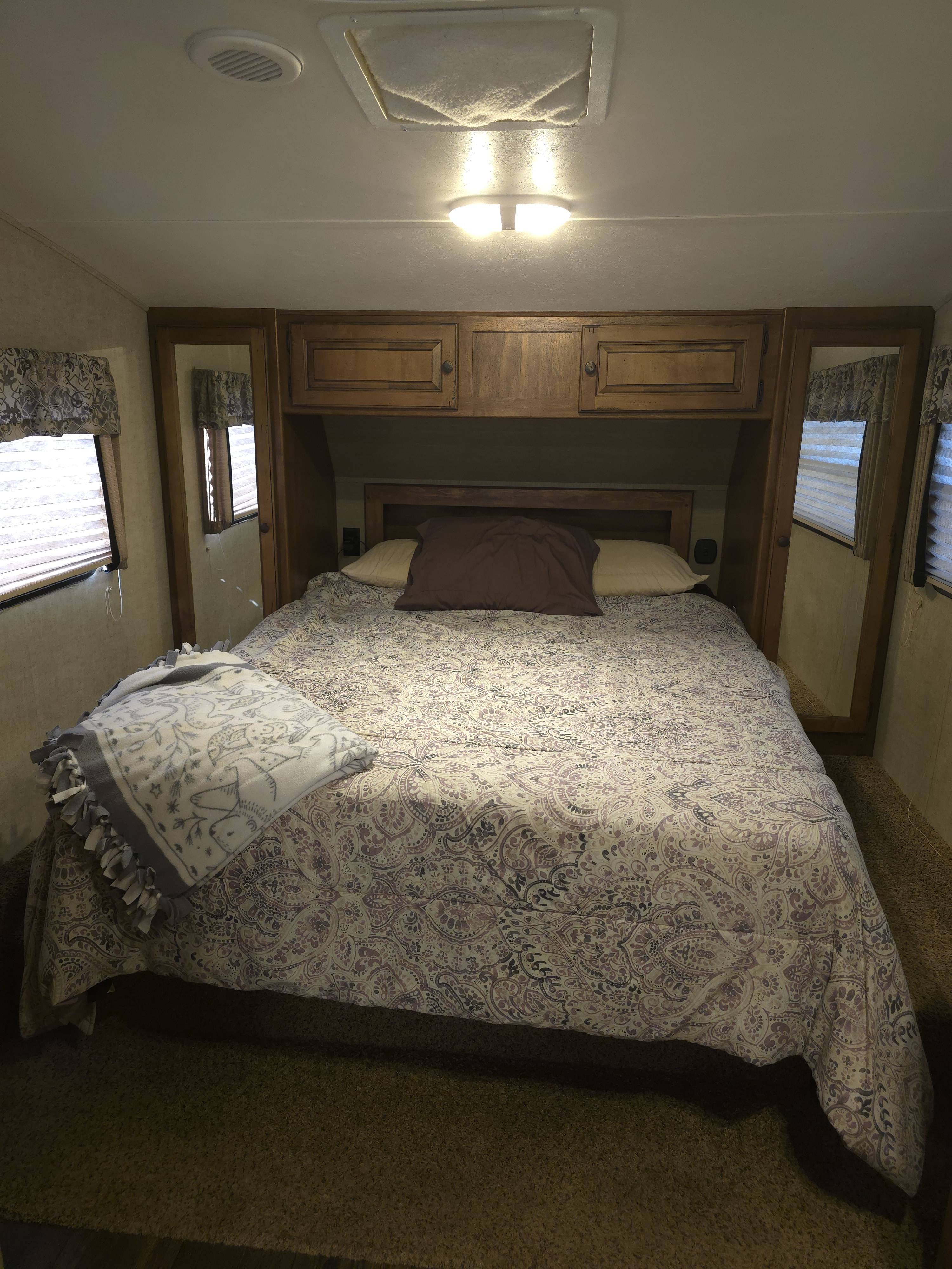 Cozy RV rental bedroom features a patterned bed, overhead cabinets, and mirrored panels, providing comfort for your travels.. Keystone RV Sprinter Copper Canyon 2013