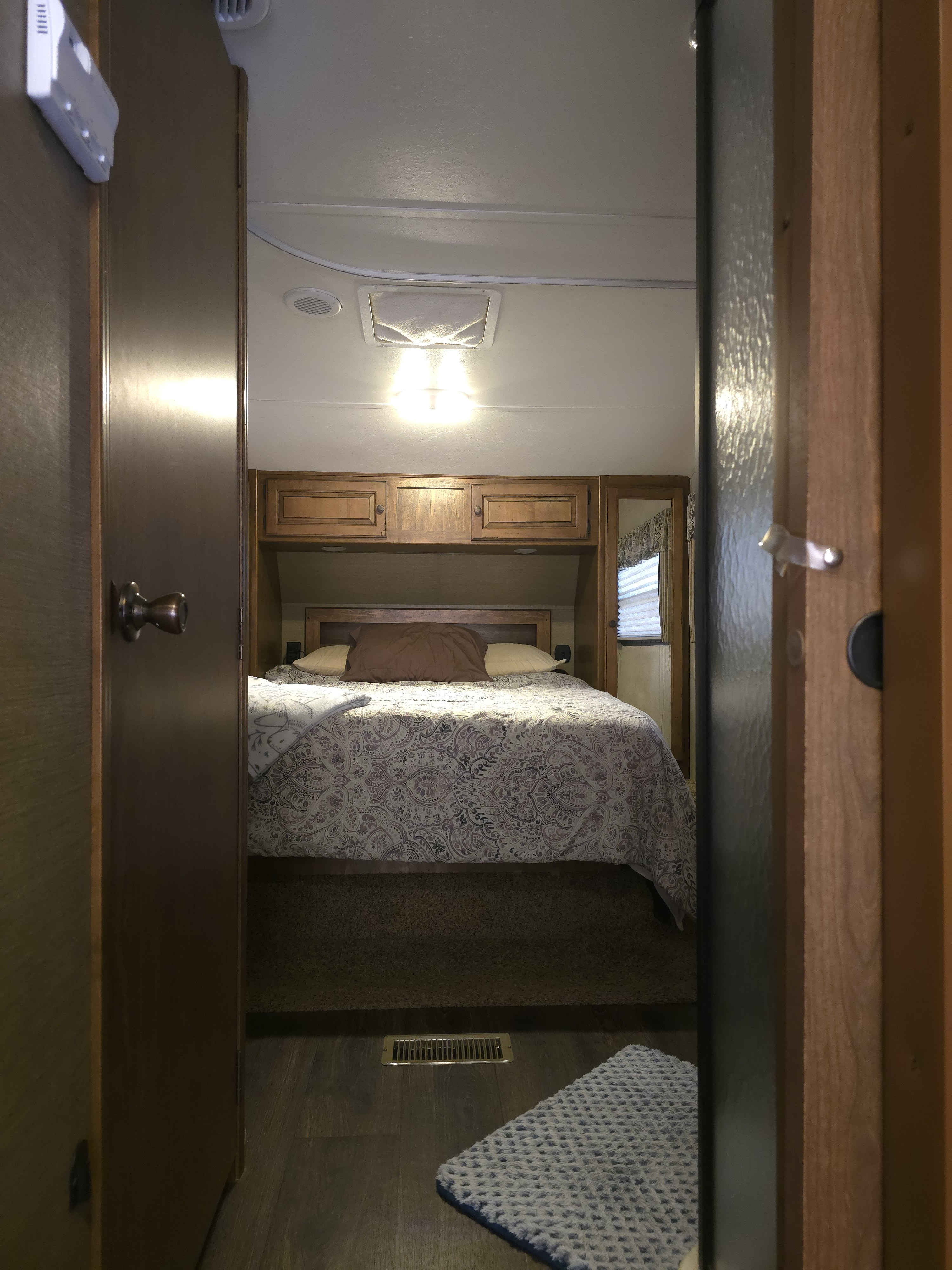 Cozy RV rental bedroom with patterned bedding & overhead storage, seen through open doors. Perfect for travel.. Keystone RV Sprinter Copper Canyon 2013