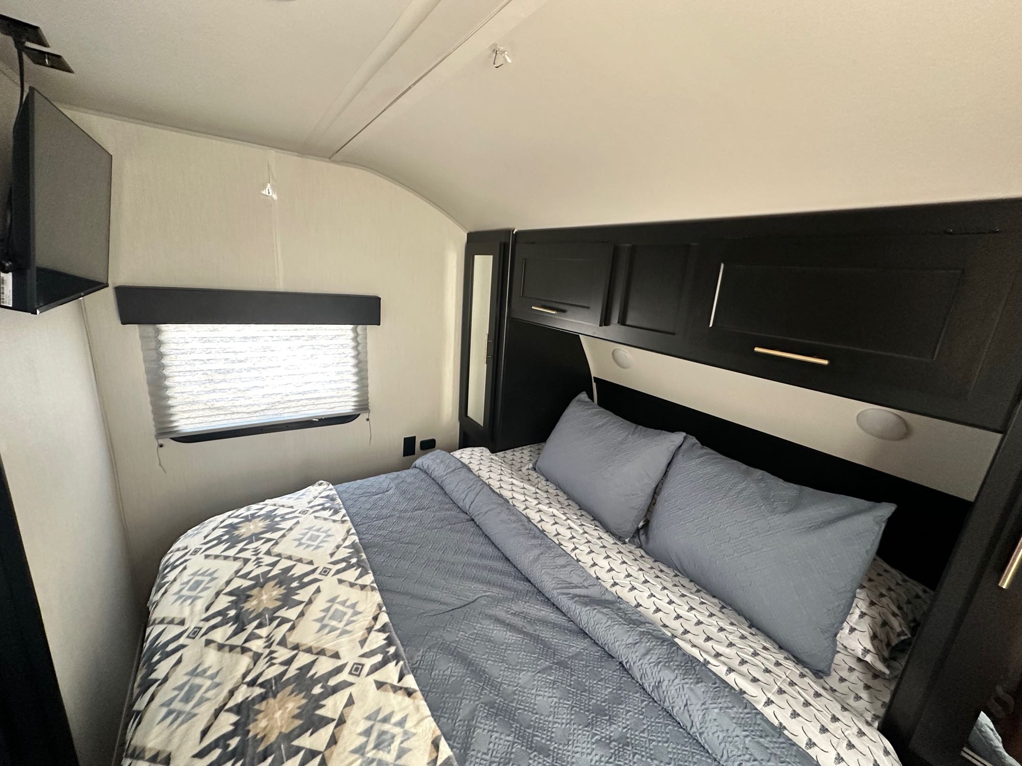 Cozy RV rental bedroom with a comfy bed, overhead cabinets, and TV, ready for your next adventure.. Forest River Cherokee Grey Wolf 2023