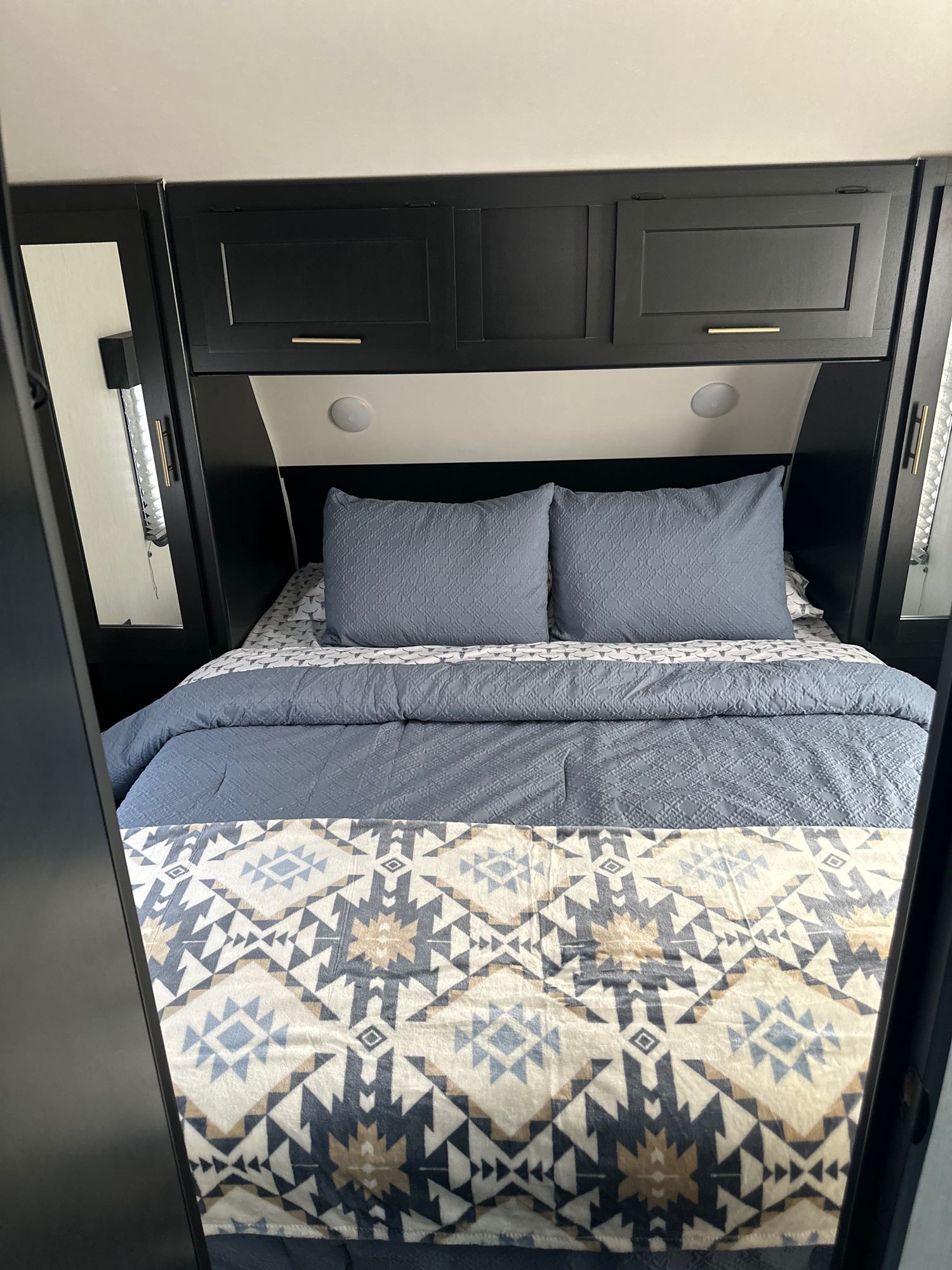 RV rental bedroom with blue bedding, a patterned blanket, and sleek overhead cabinets for comfortable travel.. Forest River Cherokee Grey Wolf 2023