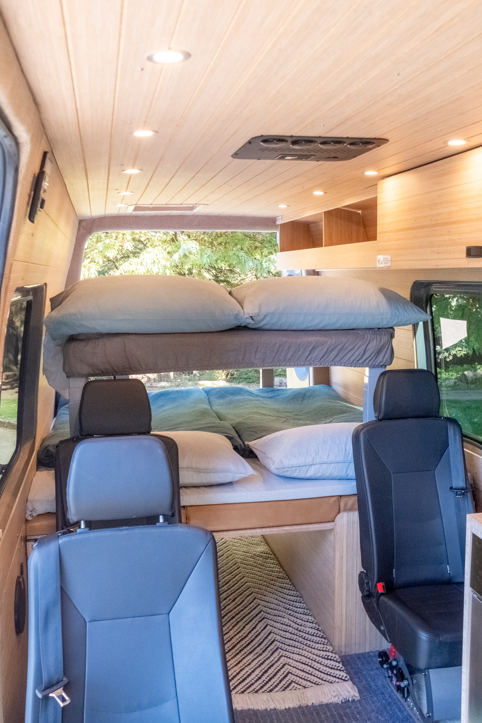 RV rental interior with cozy bunk beds, wood-paneled ceiling lights, and passenger seating. Perfect for families.. Mercedes-Benz Sprinter 2021