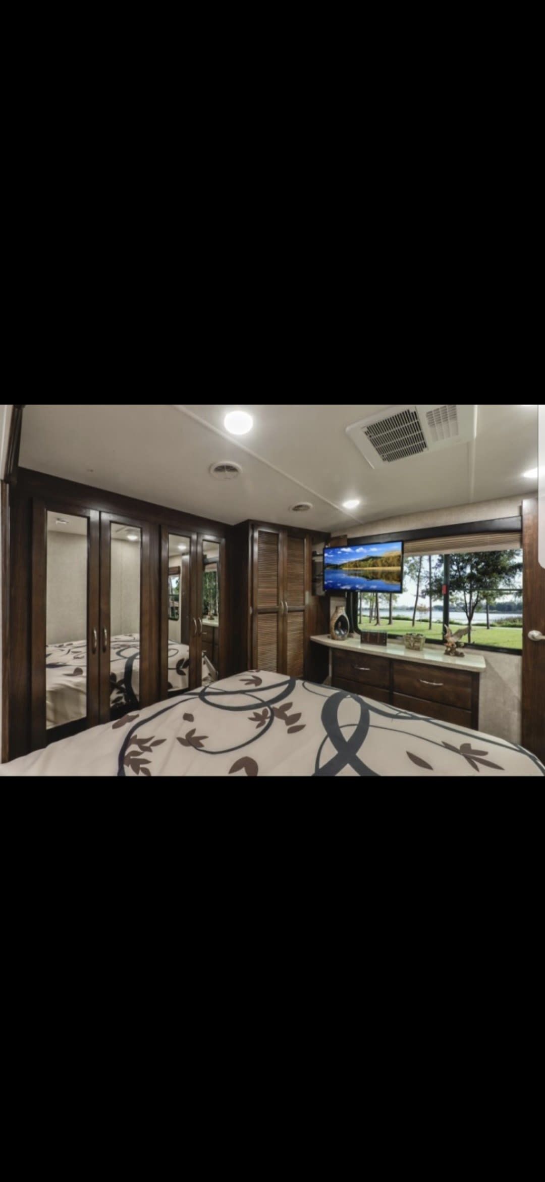 RV rental bedroom: Spacious interior with patterned bed, mirrored closets, wall-mounted TV, and scenic window view.. Heartland RVs Cyclone HD Edition Toy Hauler 2015