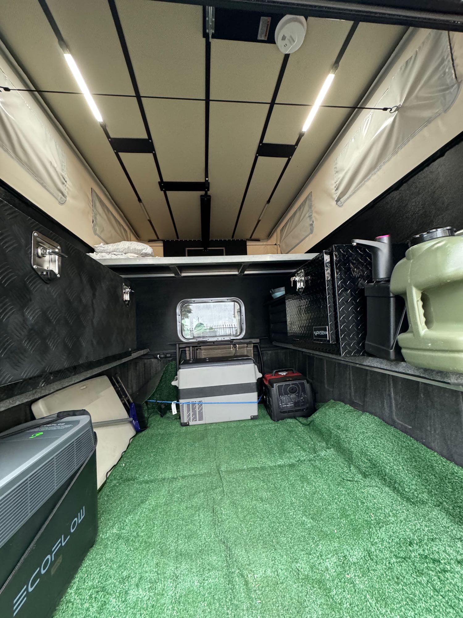 Inside an RV rental pop-top truck camper: green turf floor, ceiling lights, and essential gear like a fridge, power station, and heater.. Toyota 4wheel camper High Roof 2022