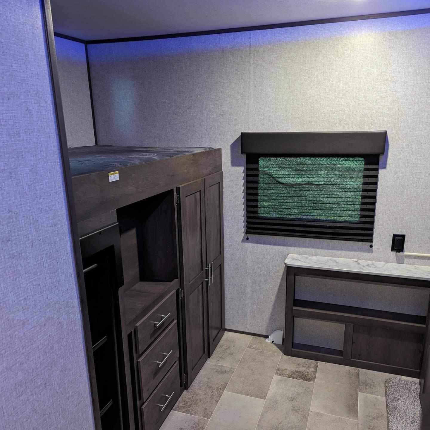 RV rental interior with dark wood bunk bed, storage, and window with blinds. Blue ceiling lights illuminate the space.. Dutchmen Coleman Lantern 2021