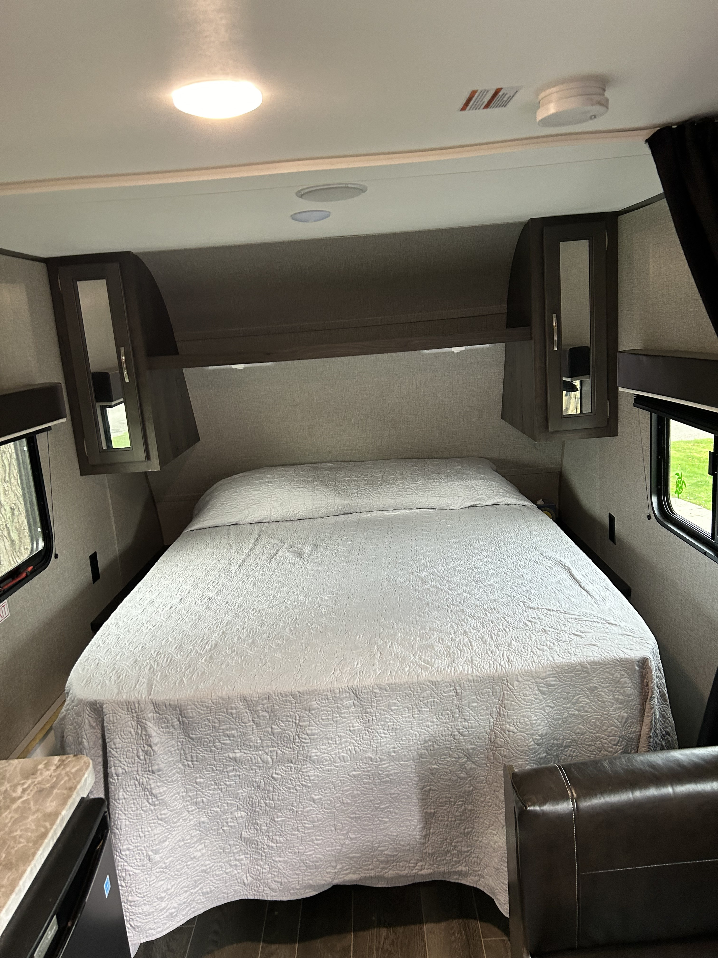 Inside an RV rental: a cozy bedroom with a quilted bed, overhead storage, and bright windows.. Jayco Jay Flight 2021