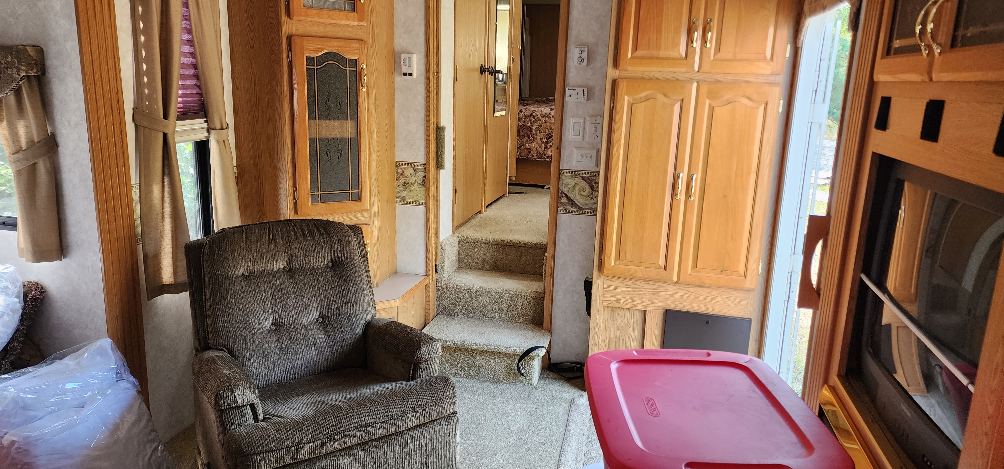 An inviting RV rental interior featuring a comfy recliner, wood cabinets, and steps leading to the sleeping area.. Keystone RV Montana 2004