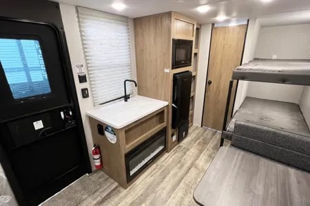 Inside this RV rental: a compact kitchen with a sink, microwave, fireplace, and bunk beds. Ideal for travel trailer adventures.. Forest River Cherokee Wolf Den EV 2024