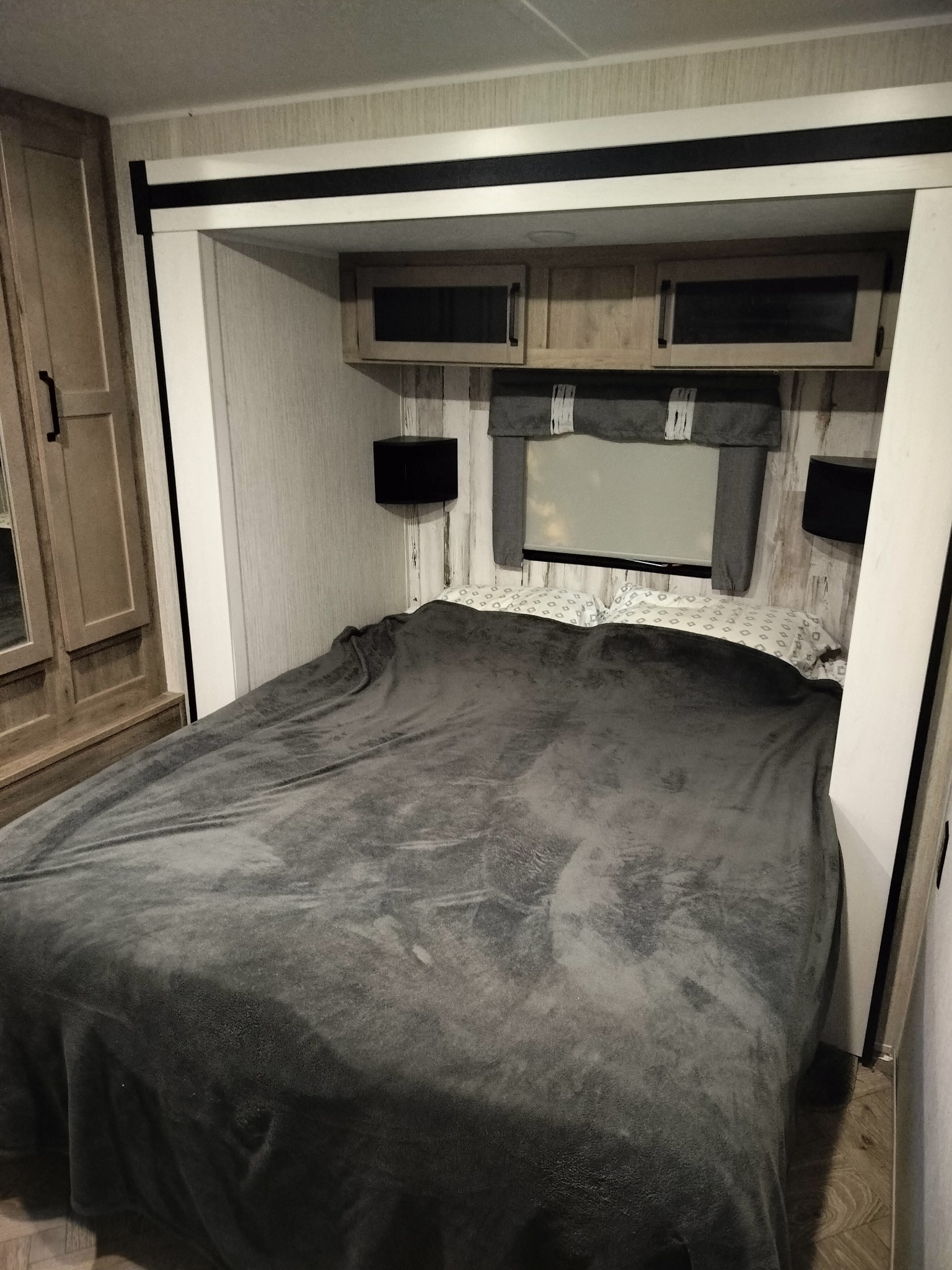 Cozy RV rental bedroom featuring a made bed with grey blanket, overhead cabinets, and a window. Perfect for your travels.. Forest River Palomino Puma 2022