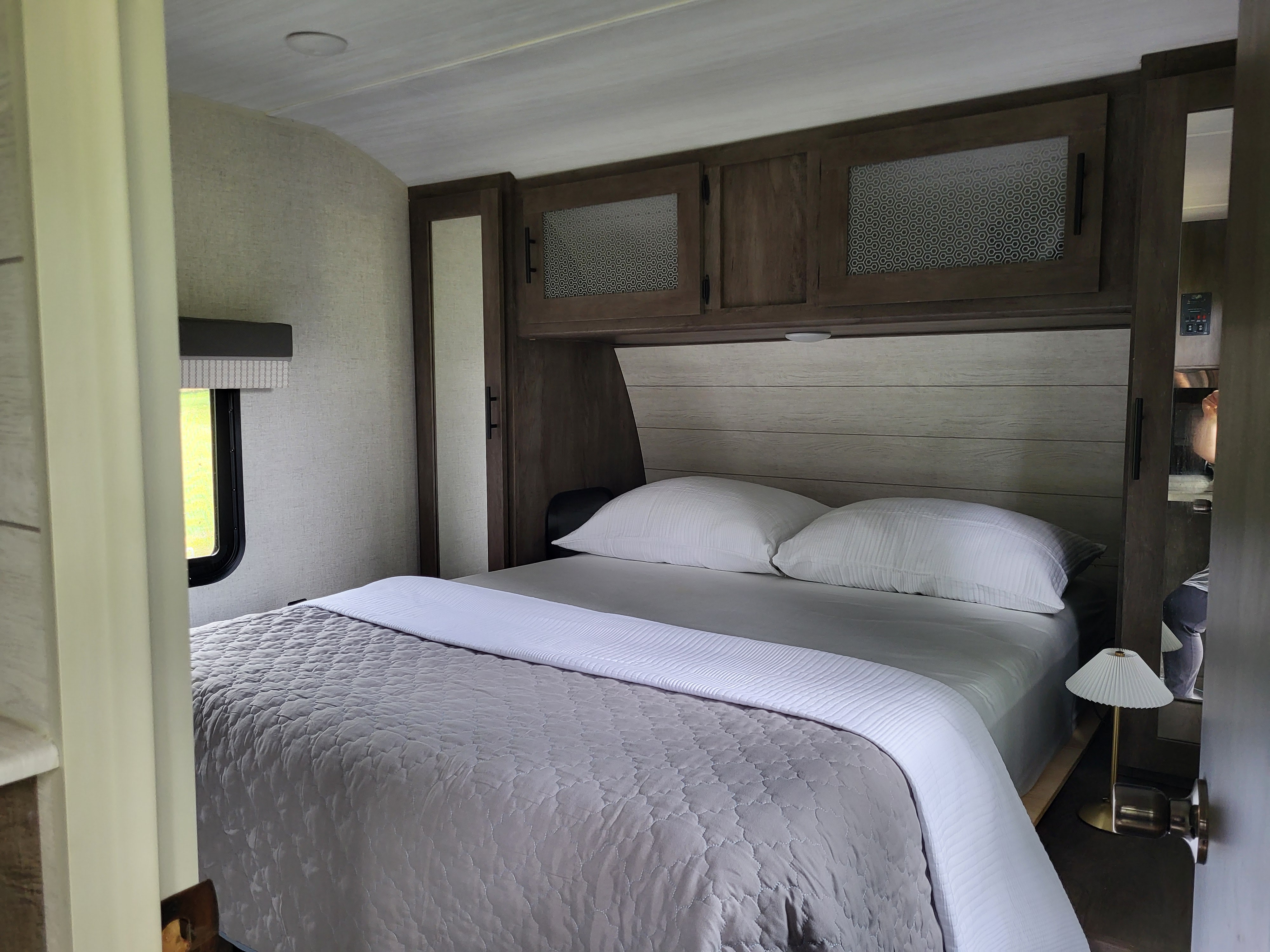 RV rental bedroom featuring a neatly made bed with white & gray linens, overhead storage, and a side window for light.. Forest River Salem 2021