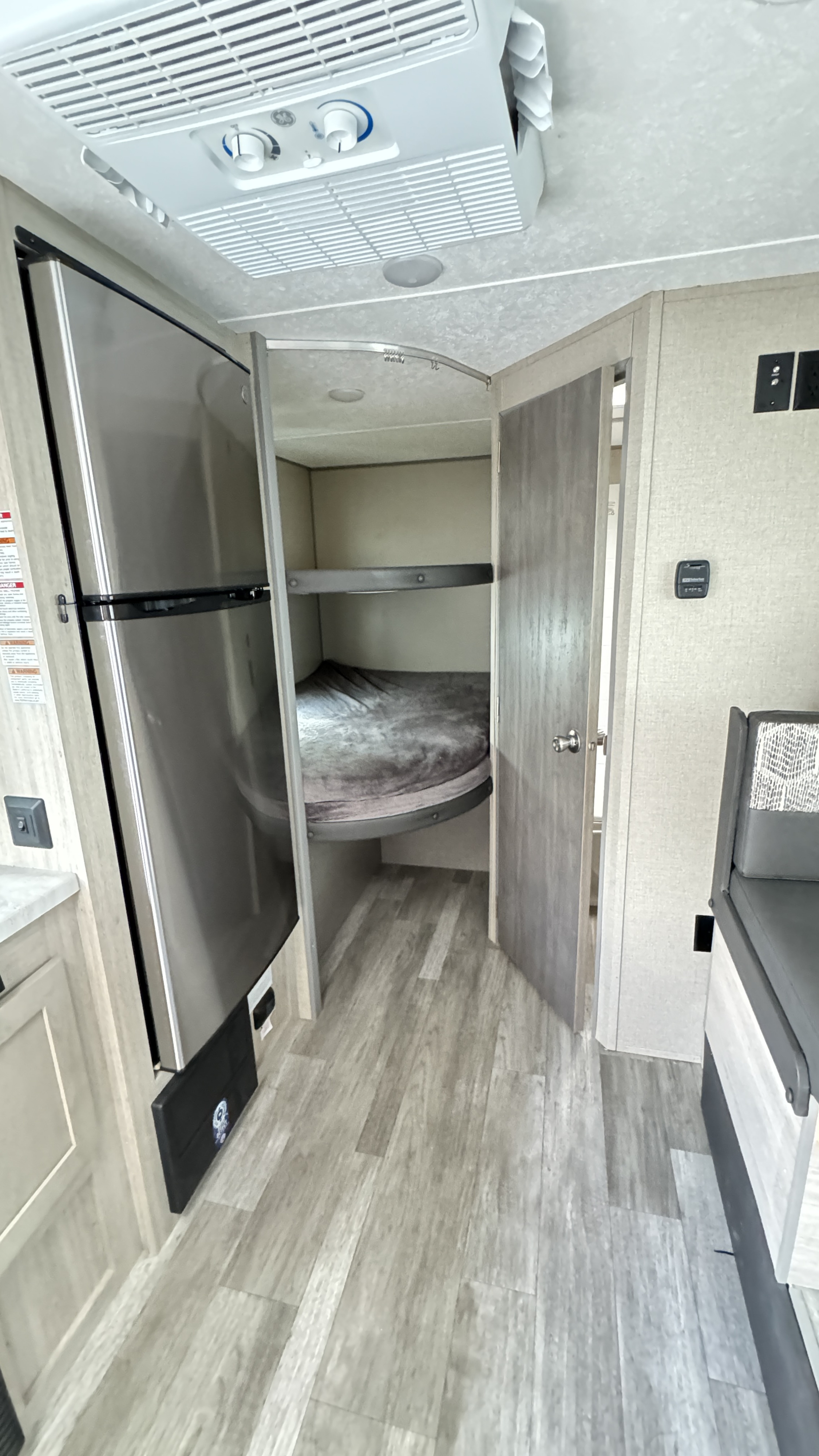 This RV rental interior showcases a large fridge, bunk beds, and an overhead AC unit, with wood-look flooring throughout.. Coachmen Catalina 2023