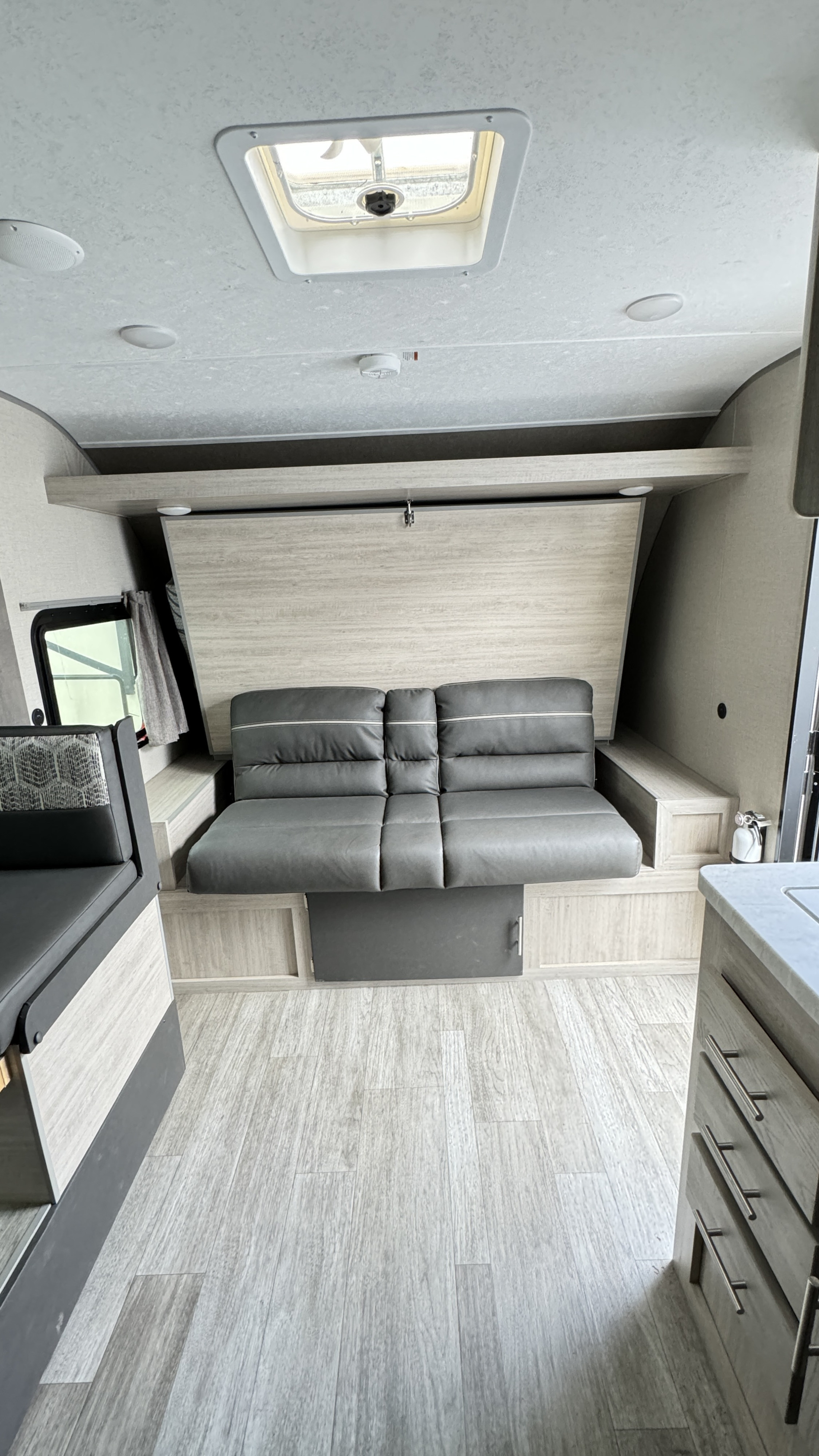 Spacious RV rental interior with a grey convertible sofa, light wood-grain walls, and ceiling skylight.. Coachmen Catalina 2023