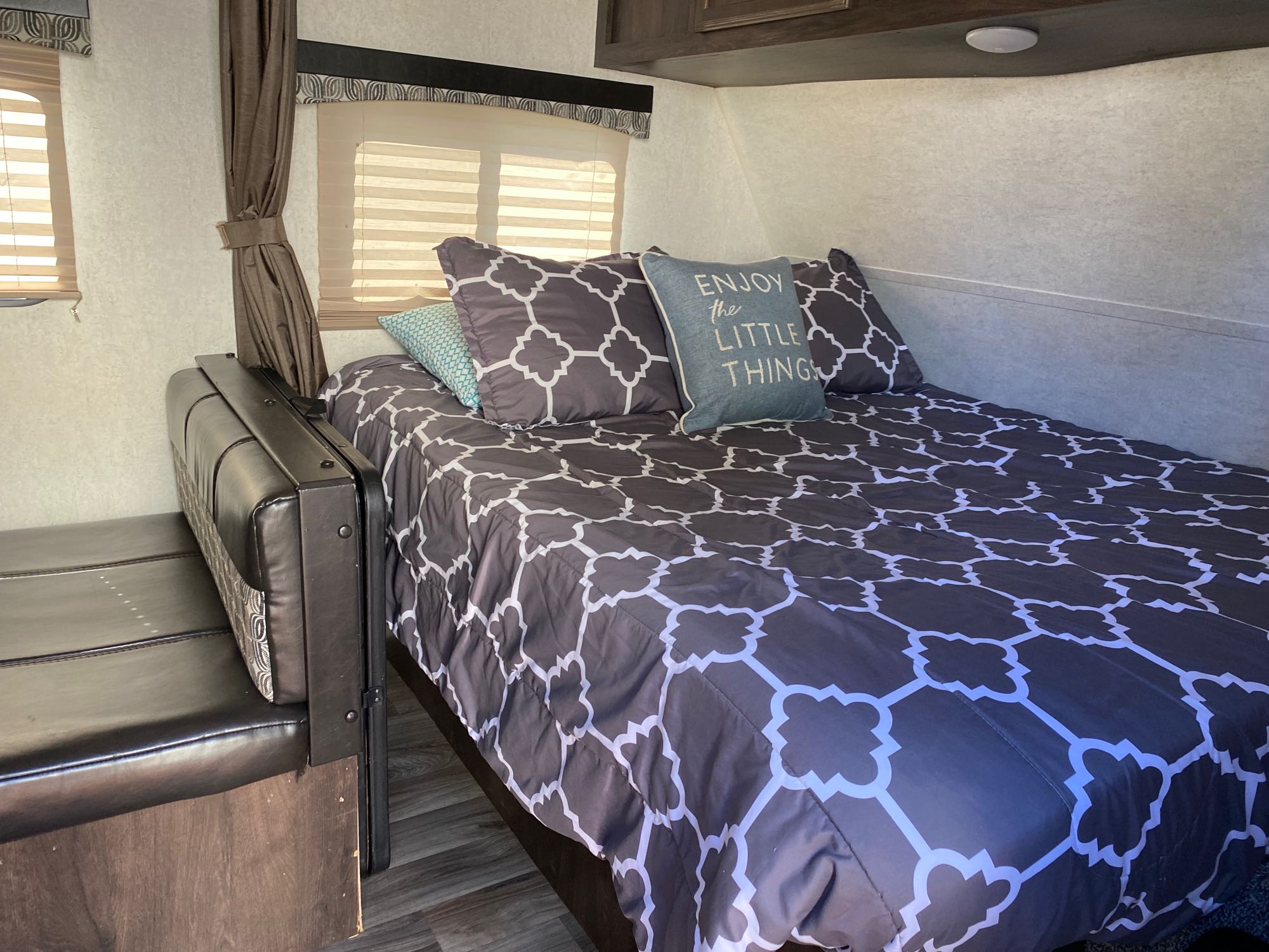 An RV rental bedroom setup with a stylish bed, "Enjoy the Little Things" pillow, and black bench, ready for travel.. Starcraft Autumn Ridge 2018