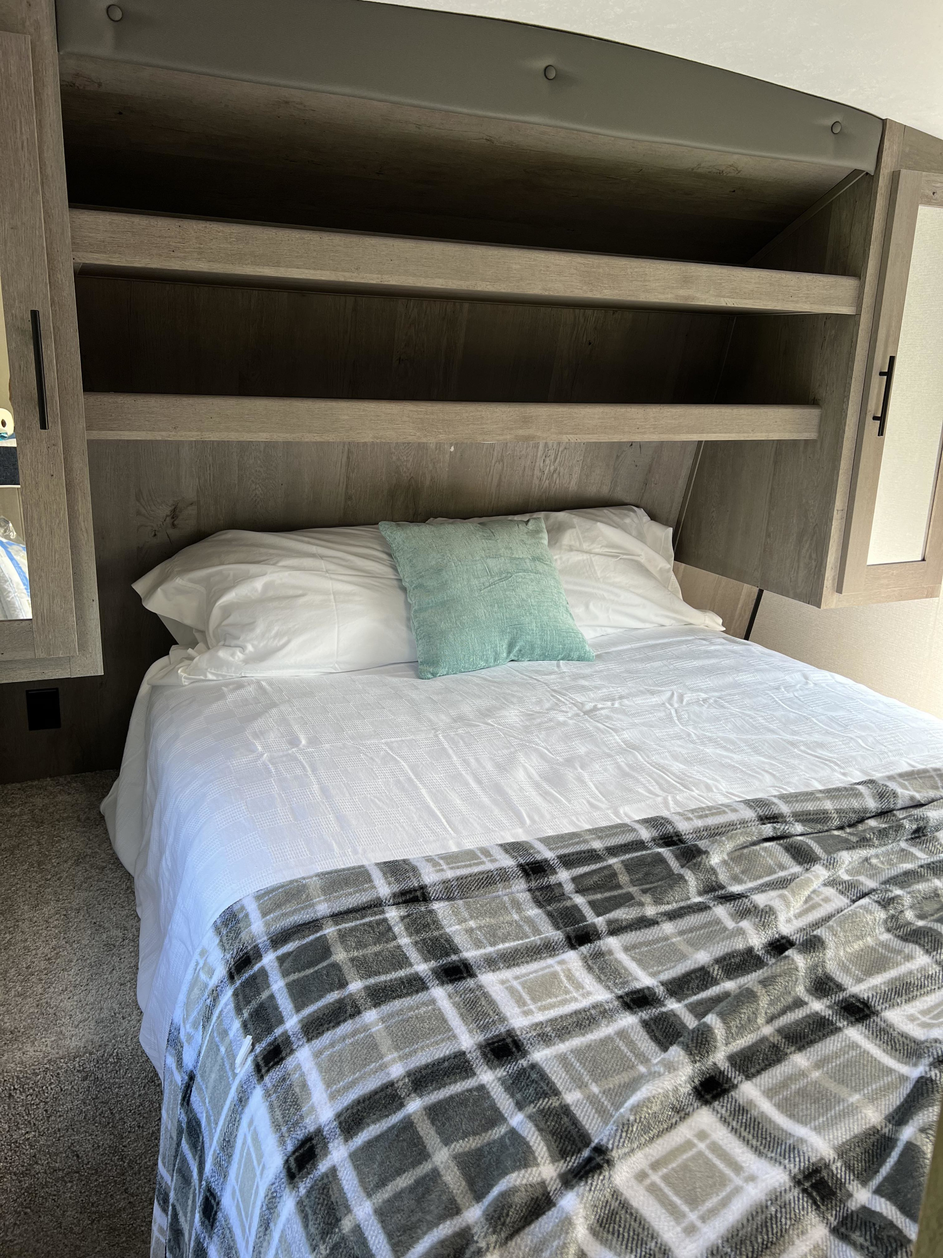Cozy RV rental bedroom with a comfortable bed, white bedding, plaid blanket, and built-in storage. Ideal for travel.. Keystone RV Springdale 2021
